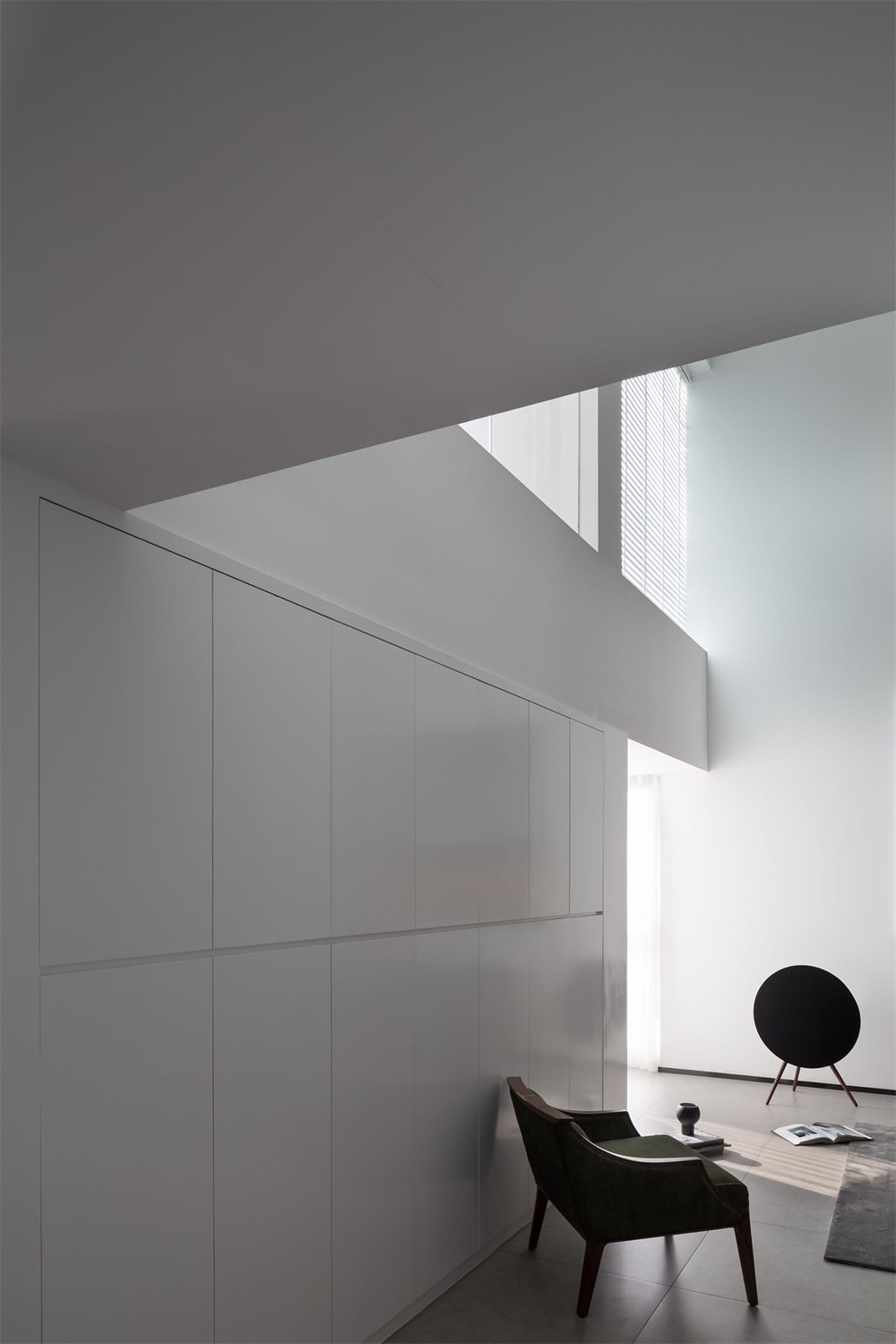Modern, white, concrete interior space with minimalist design and green armchair.