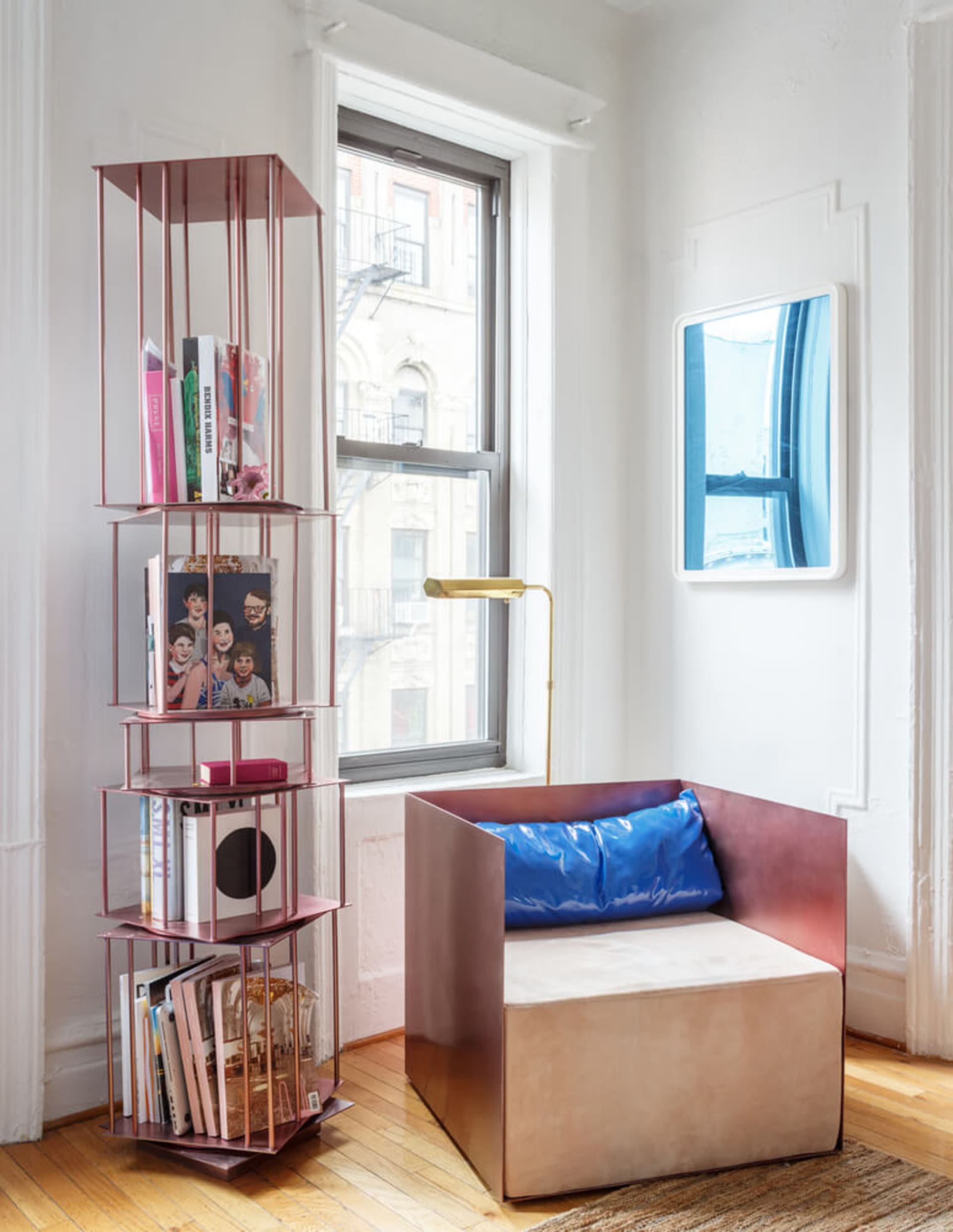 A minimalist living room featuring a metallic bookshelf, a comfortable chair with a blue cushion, and a framed window view.