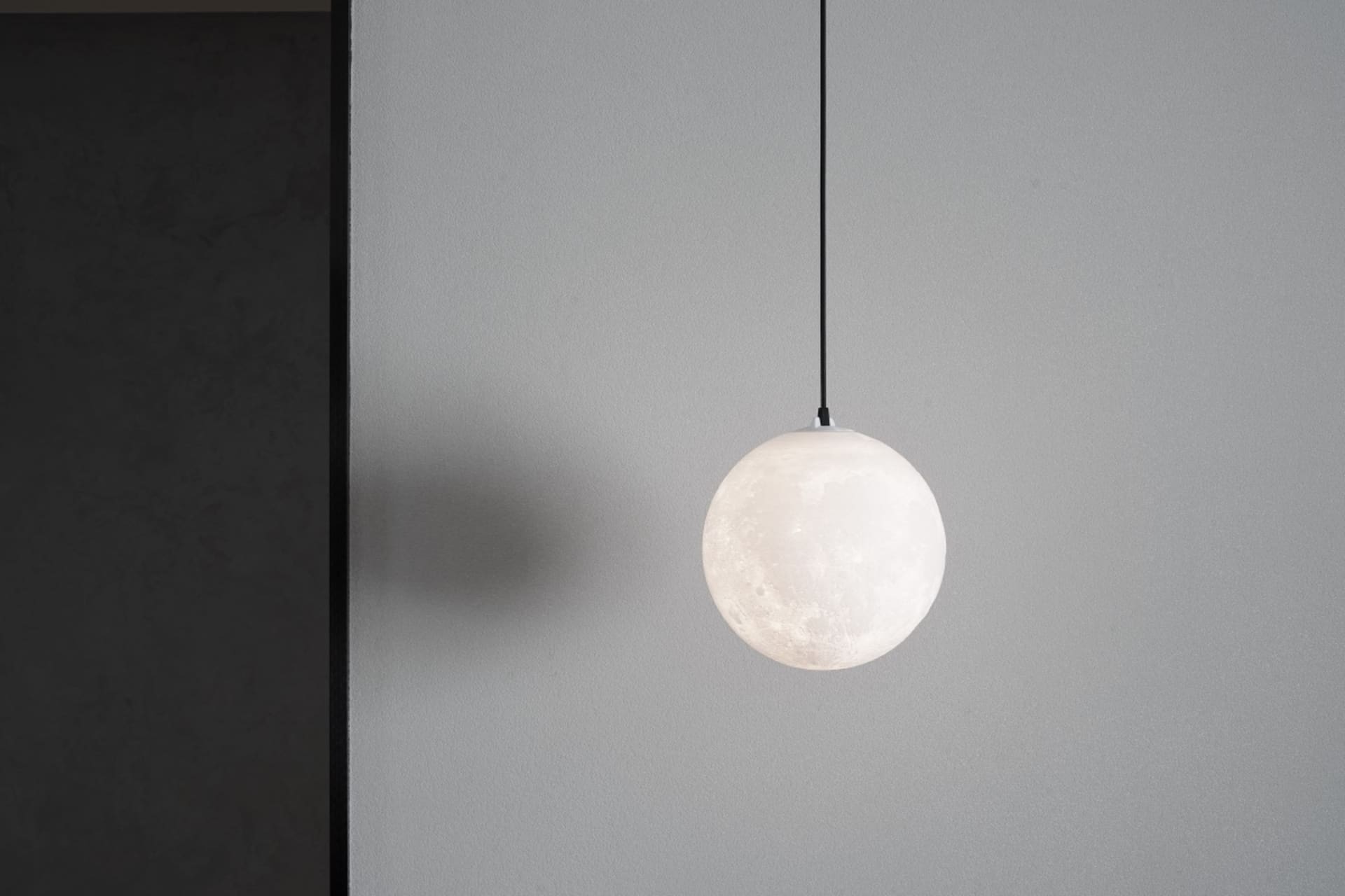 A minimalist glass sphere pendant light hanging from a black cord against a gray wall.