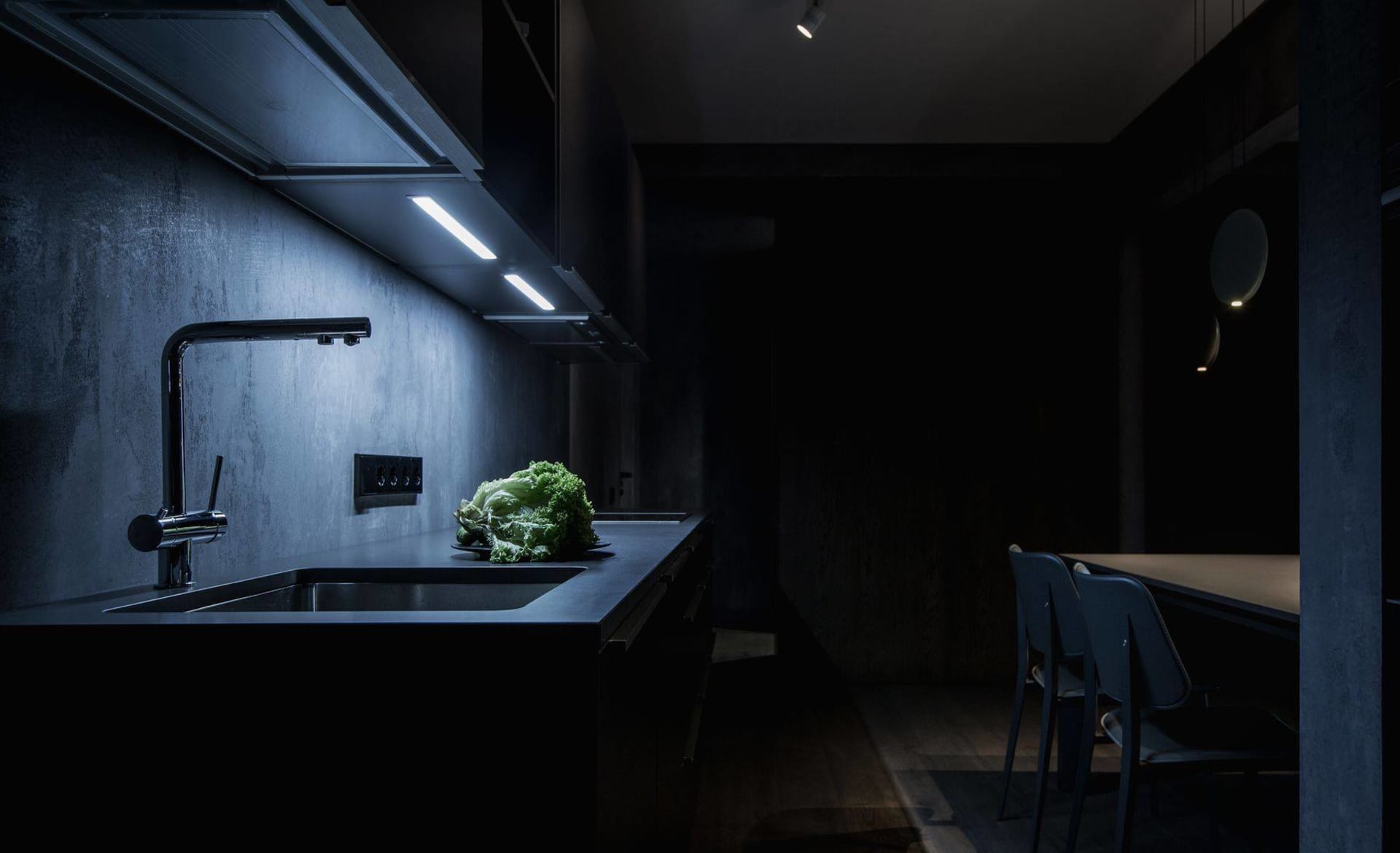 A modern, minimalist kitchen with black countertops and a concrete backsplash.