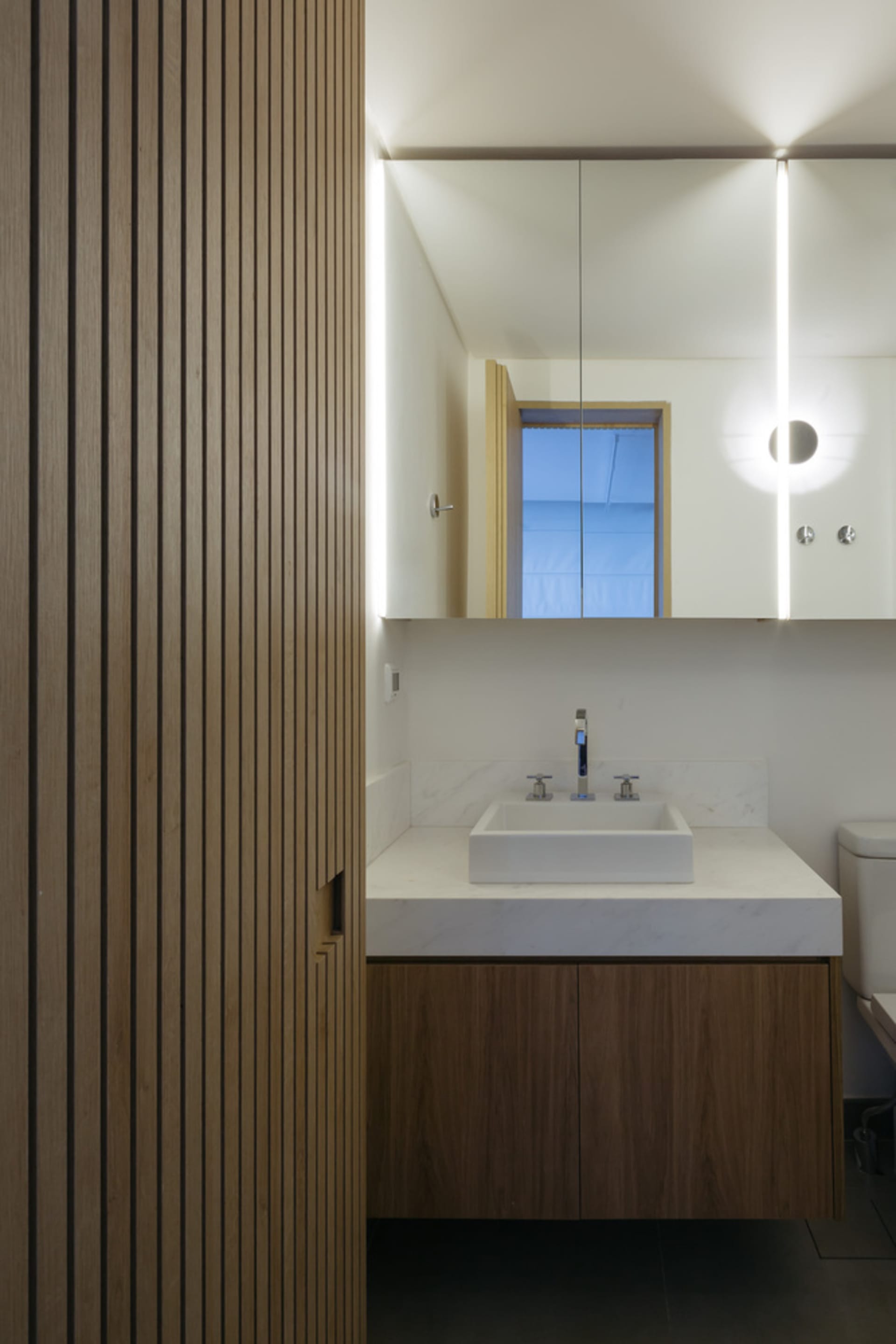 A modern bathroom featuring minimalist wood accents and a sleek white countertop sink.