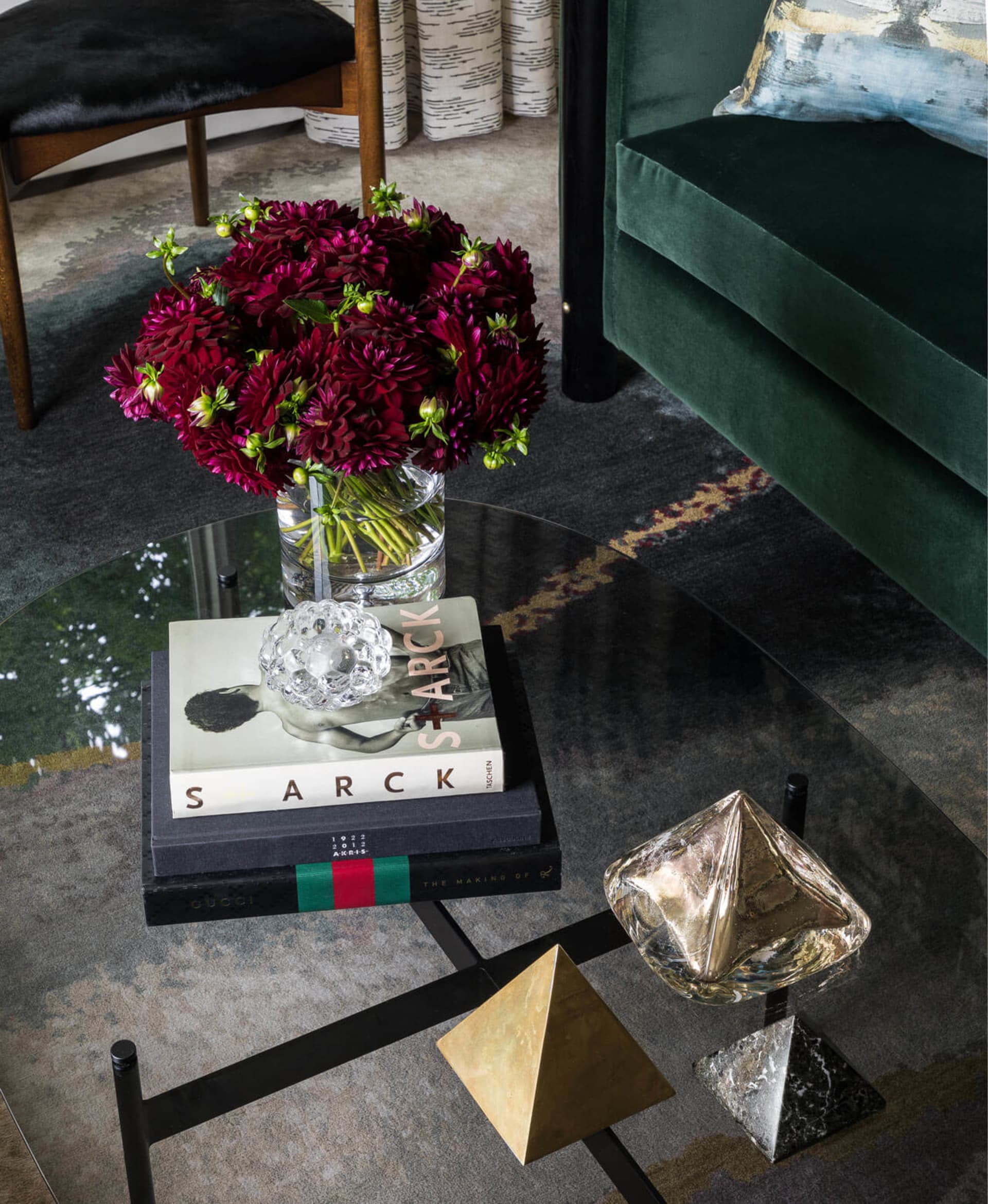 A modern living room featuring glass coffee table, velvet couch, metal side table, and decorative elements on the floor.
