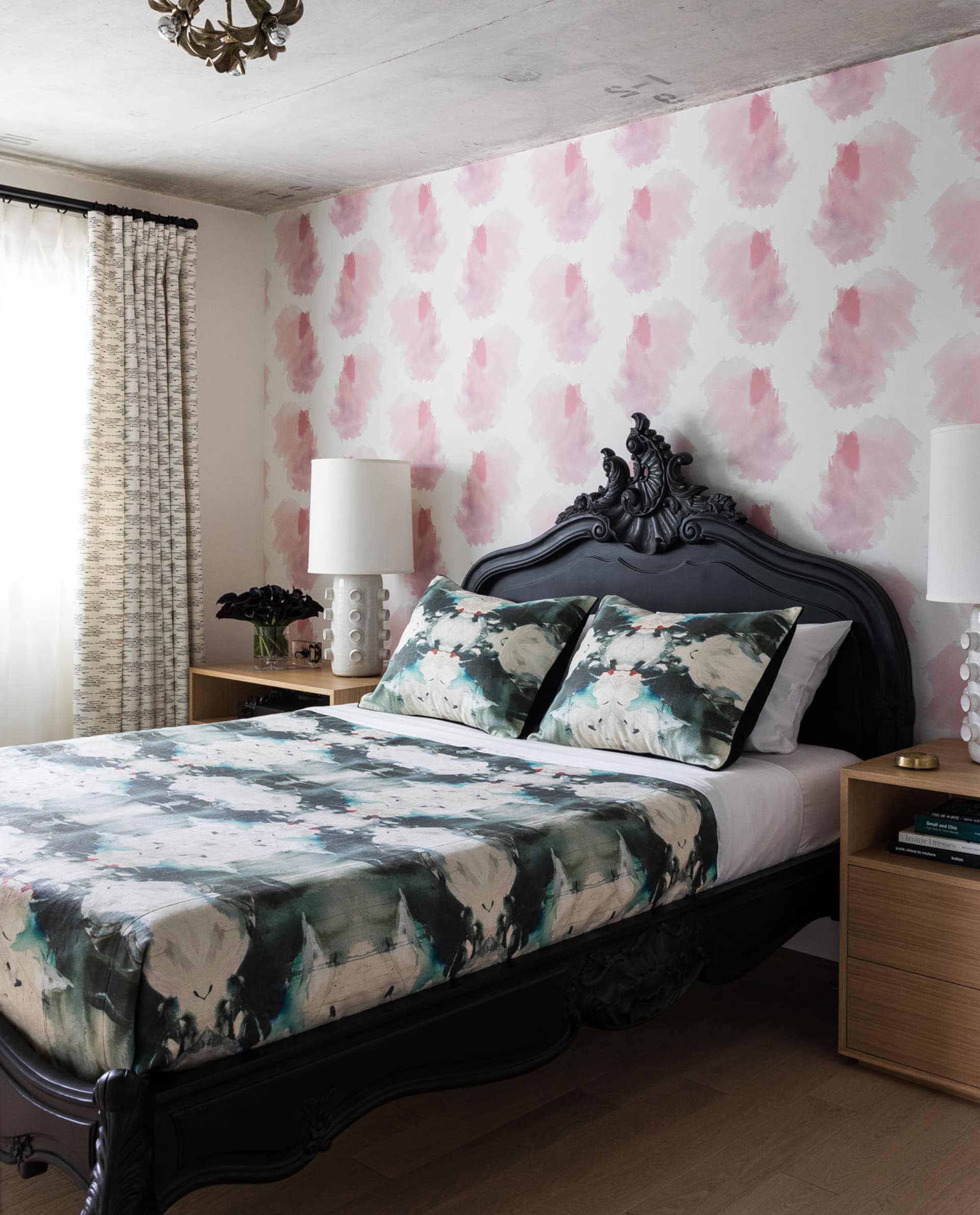 A modern bedroom featuring a bed with patterned bedding and a headboard, against a wall with pink and white patterned wallpap