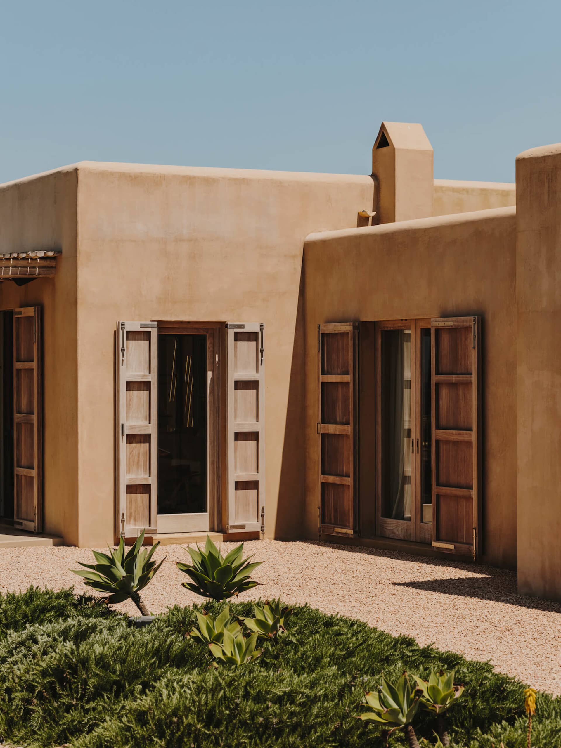 A modern building with earth-toned walls and large wooden doors and windows.