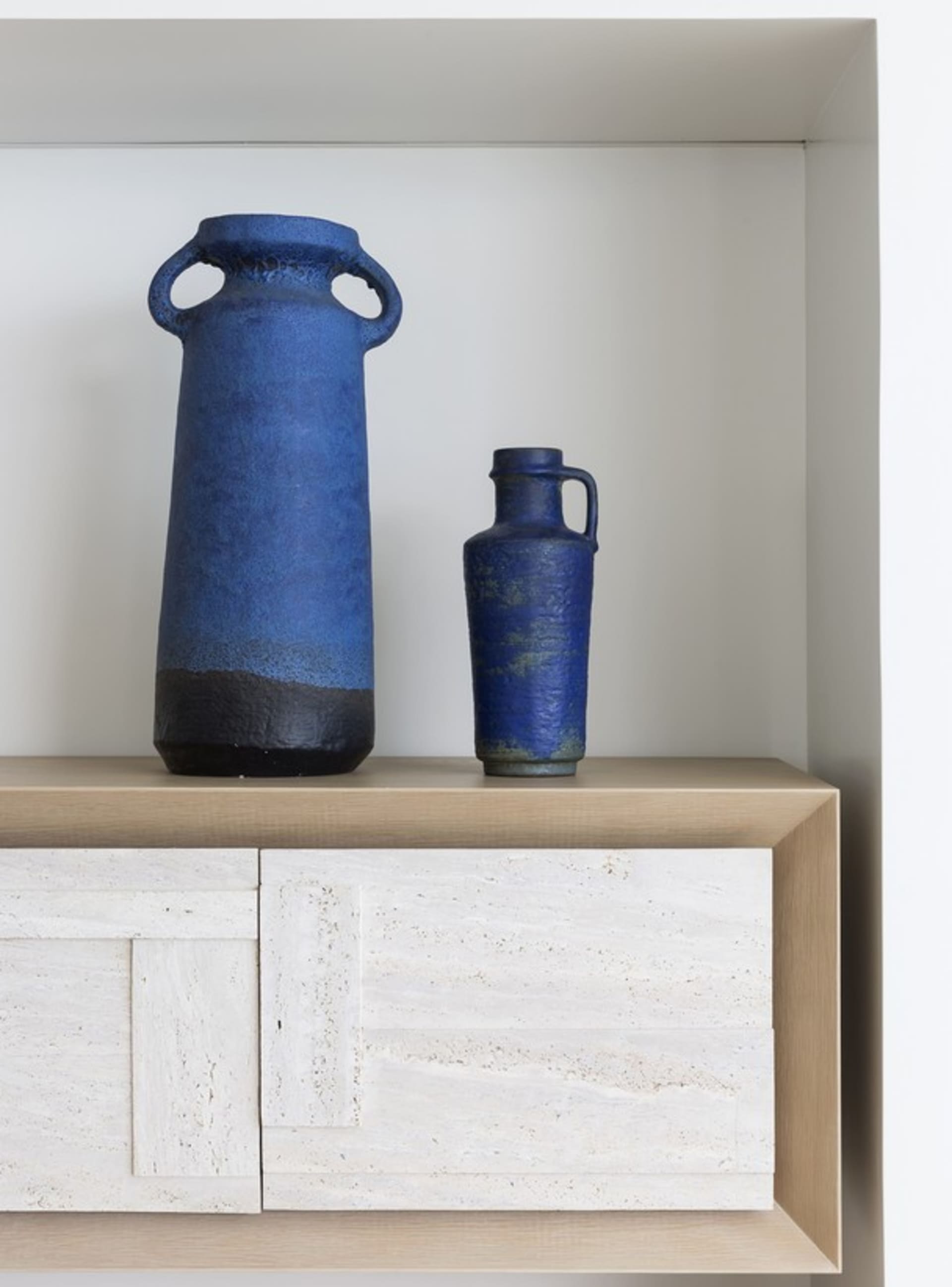 Two blue ceramic vases with a matte finish, placed on a wooden sideboard.