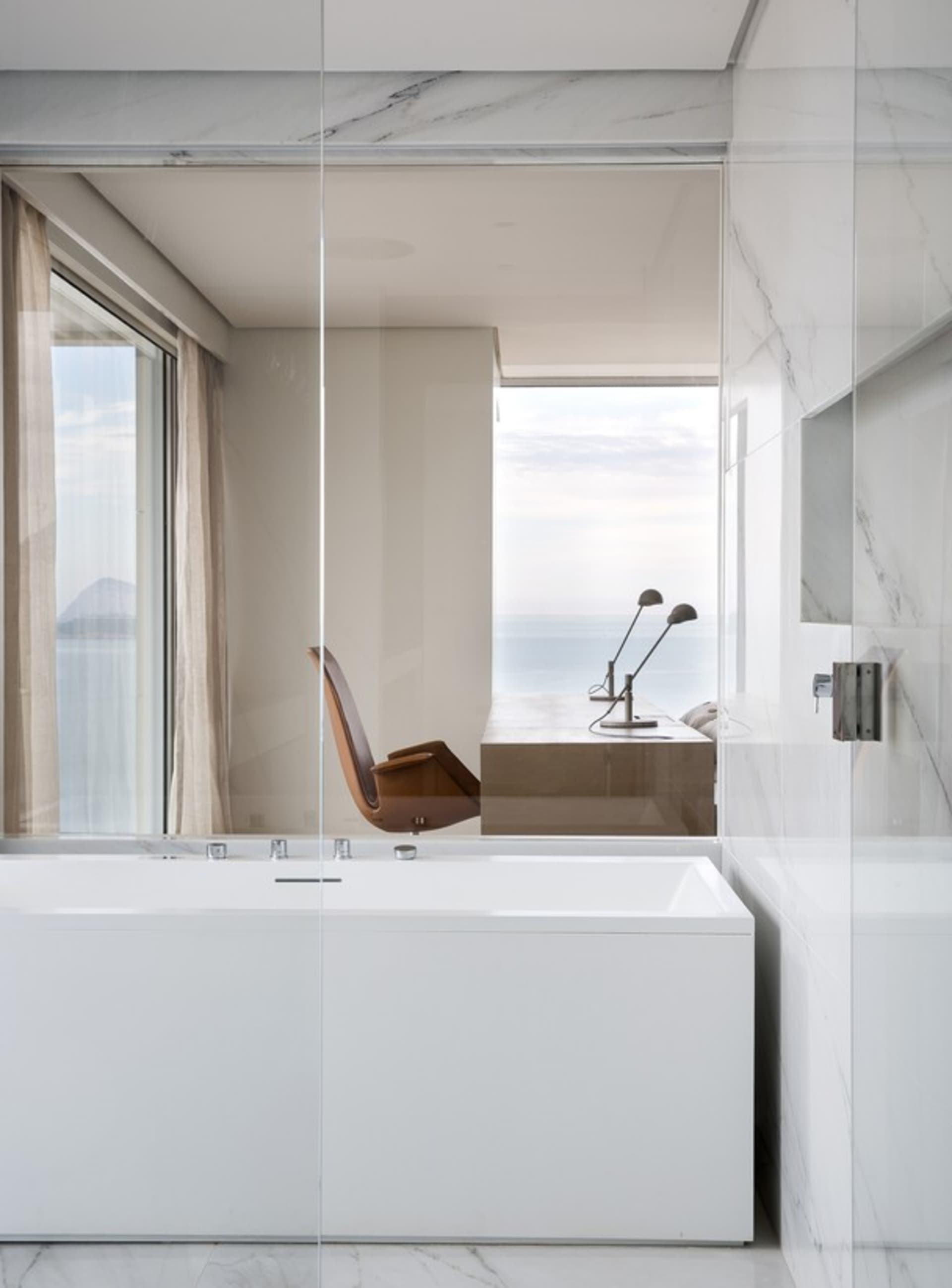 A minimalist bathroom featuring a white marble bathtub with an ocean view.