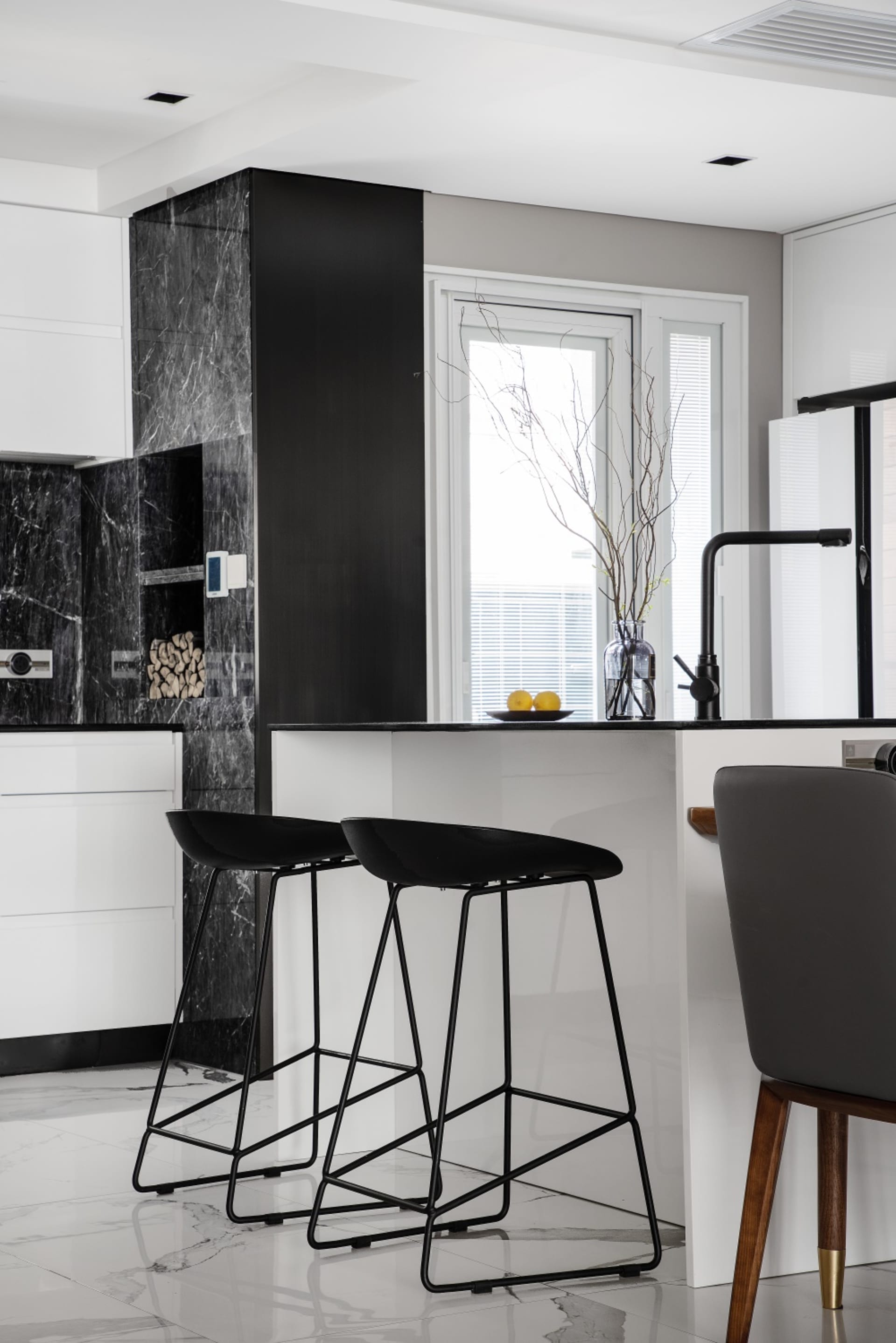 Modern kitchen with black and white marble countertops and black stools.