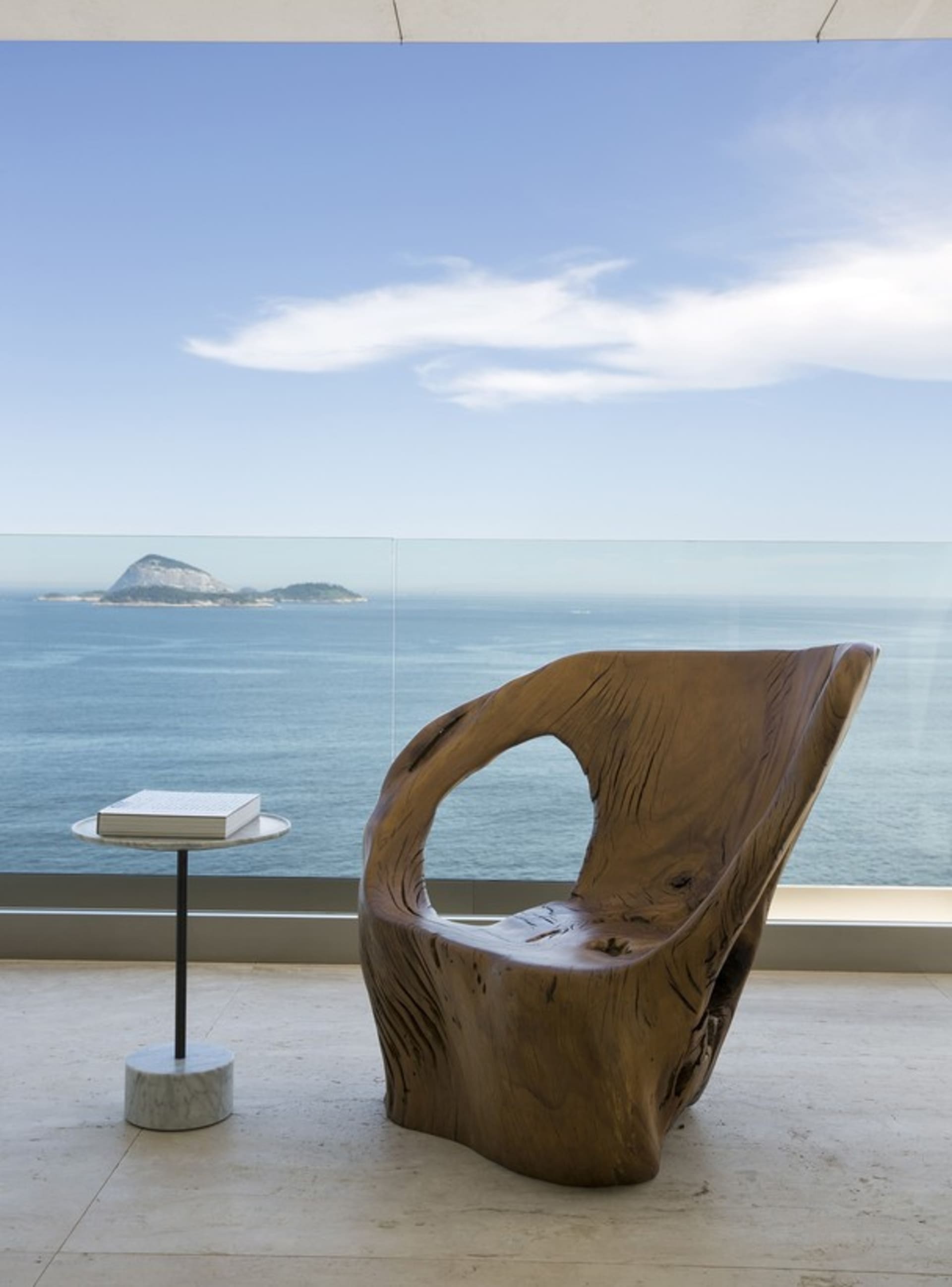 Modern, sleek lounge chair crafted from textured, dark wood on a sleek, minimalistic patio overlooking the ocean.