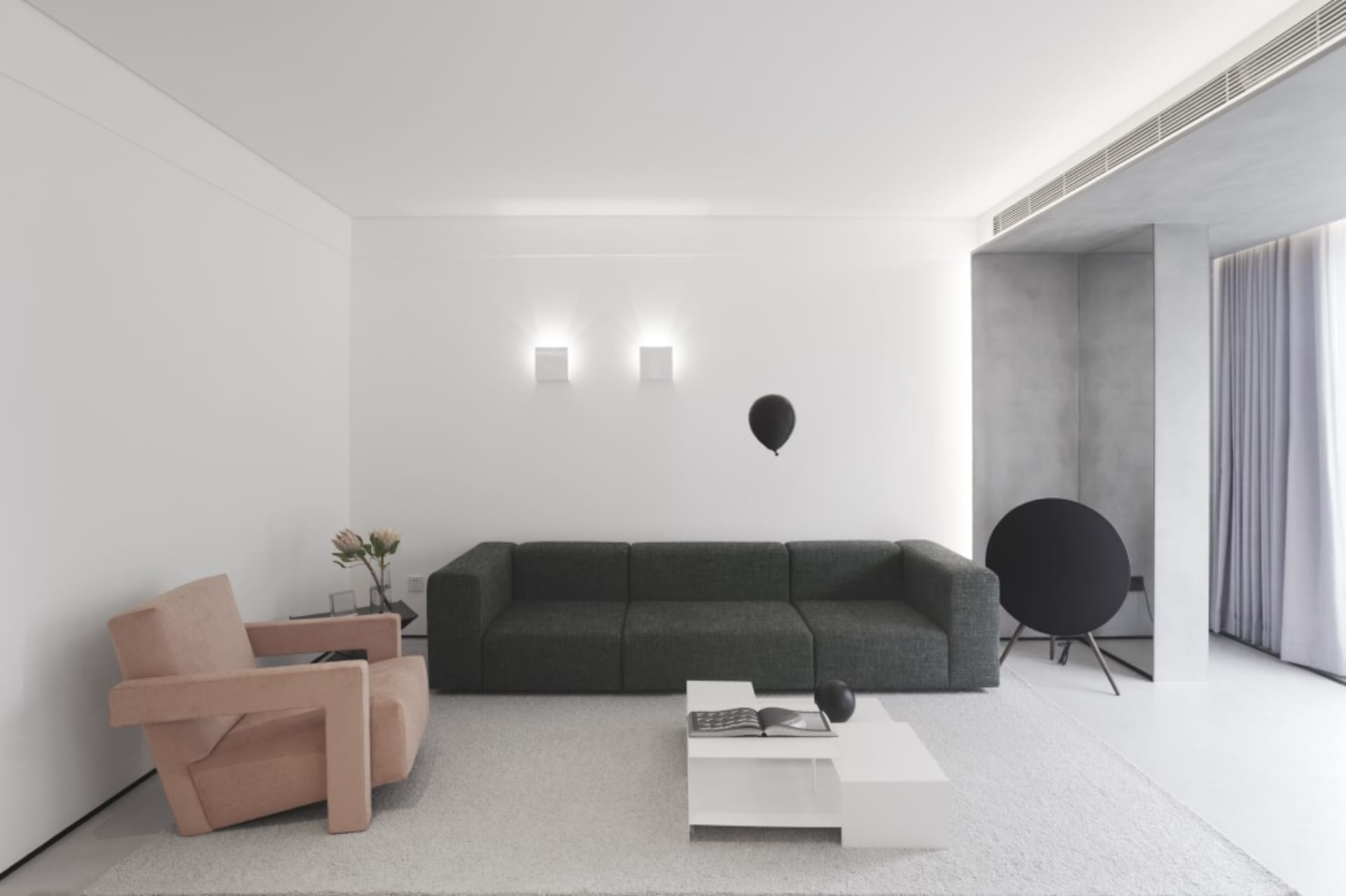 A minimalist living room featuring a gray sofa, a white coffee table, and a pink armchair.