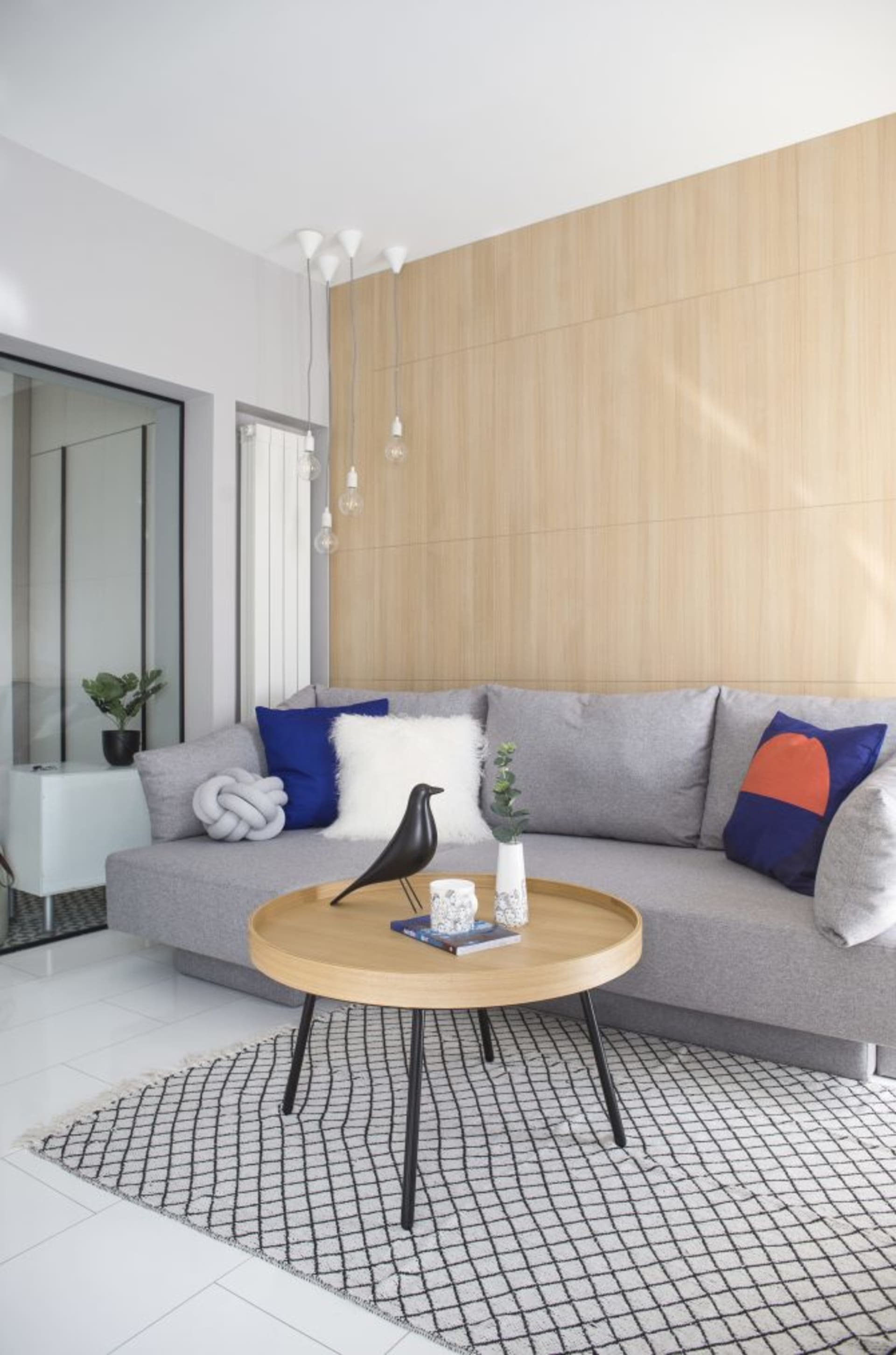 A modern living room with a gray sectional couch, round wooden coffee table, and blue and orange decorative pillows.