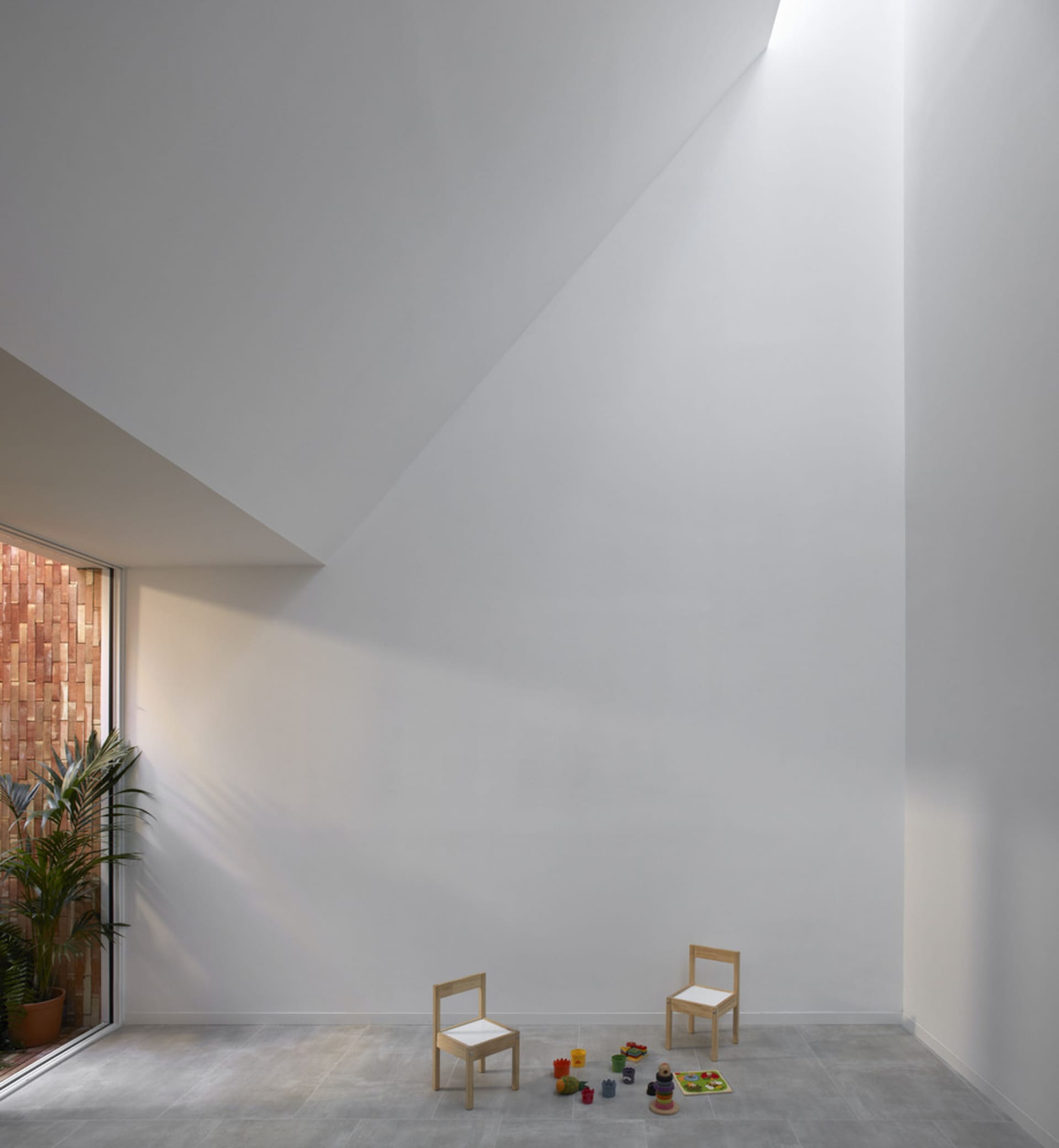 White steel and concrete floor with two small wooden chairs and children's toys in a minimalist play area.