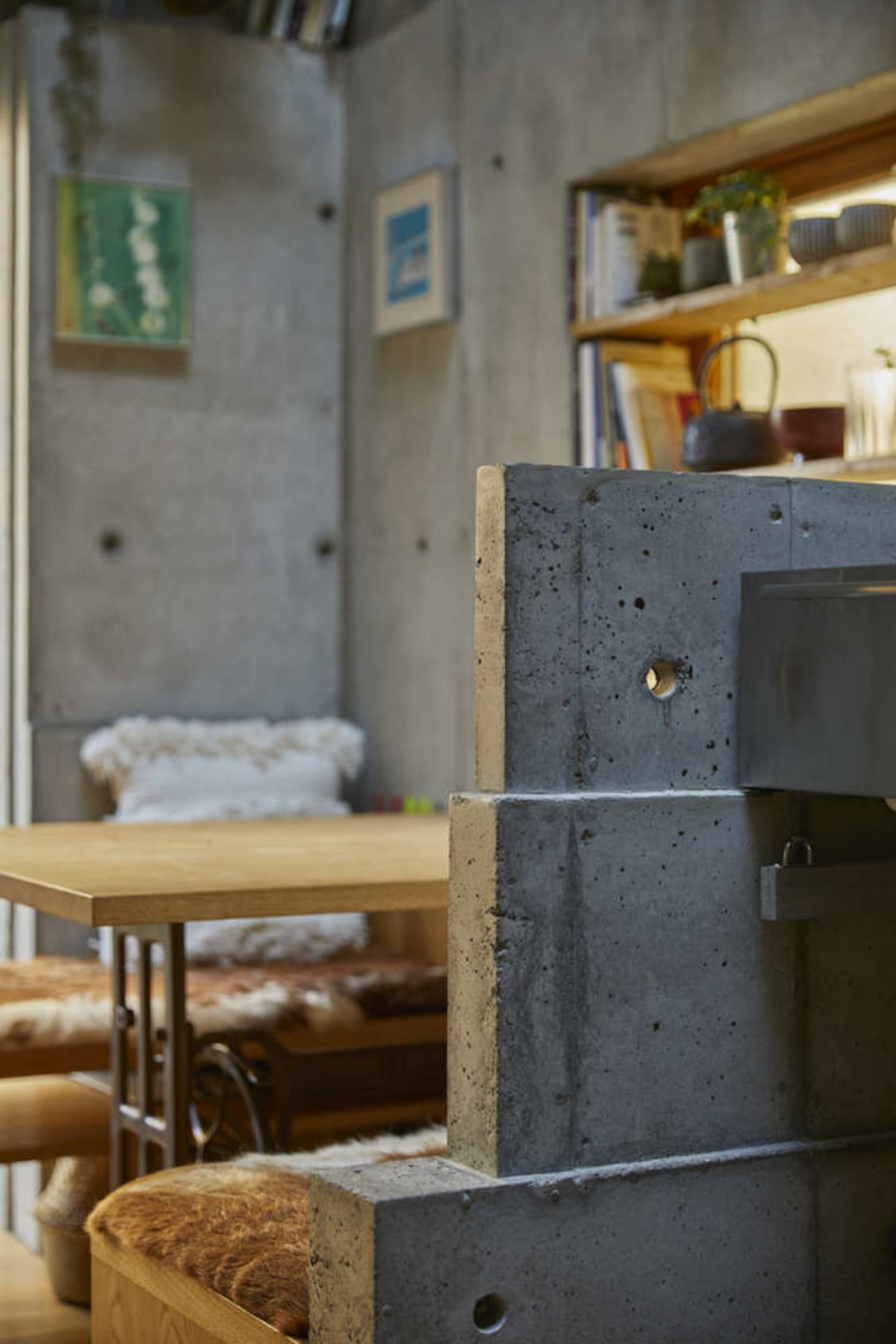 A close-up of a modern industrial living room with a prominent concrete fireplace and wooden seating.
