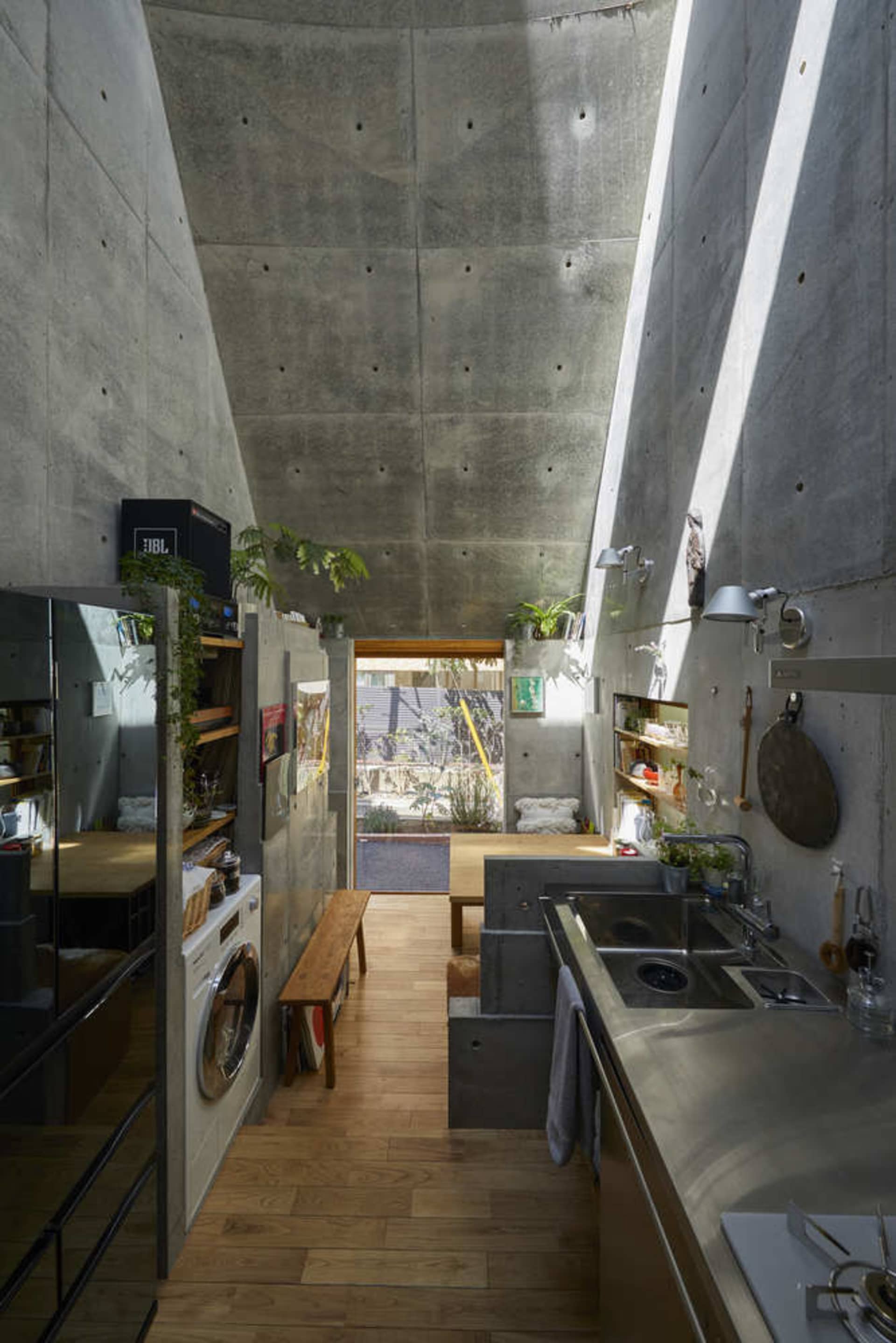 Modern minimalist kitchen with a concrete ceiling and floor, featuring a sink, stove, and washing machine