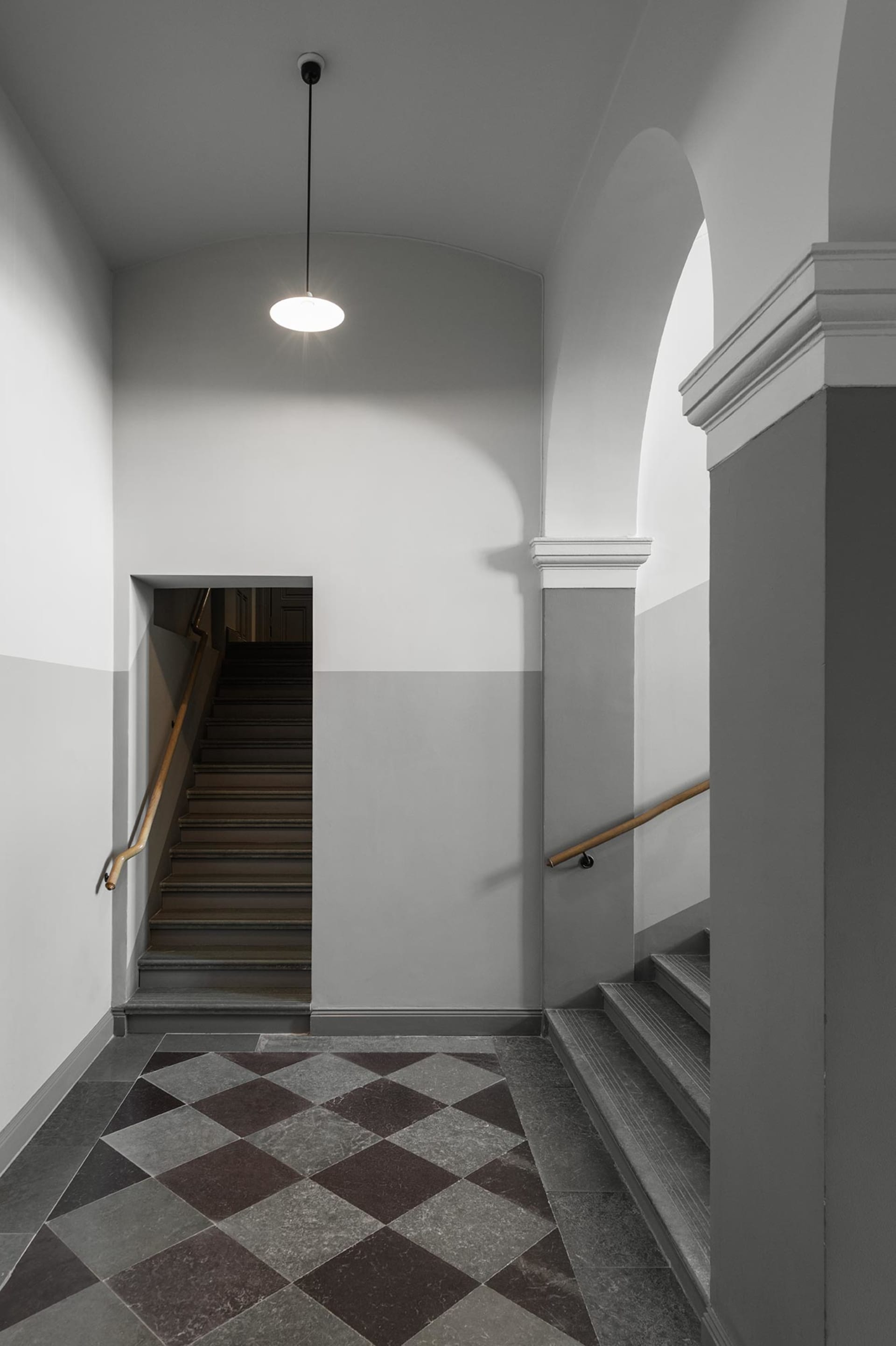 A modern interior hallway with concrete tiles, archways, and stairs.