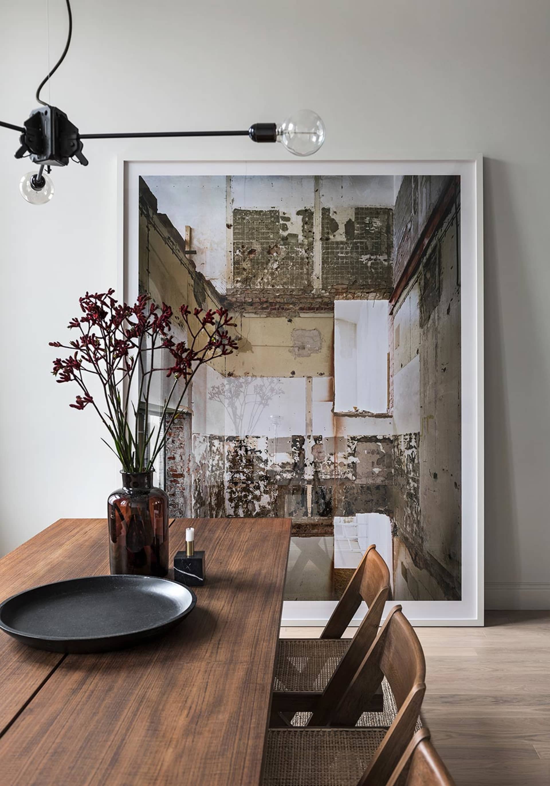 A modern dining room with wooden furniture, a vase with flowers, and a framed architectural photograph on the wall.