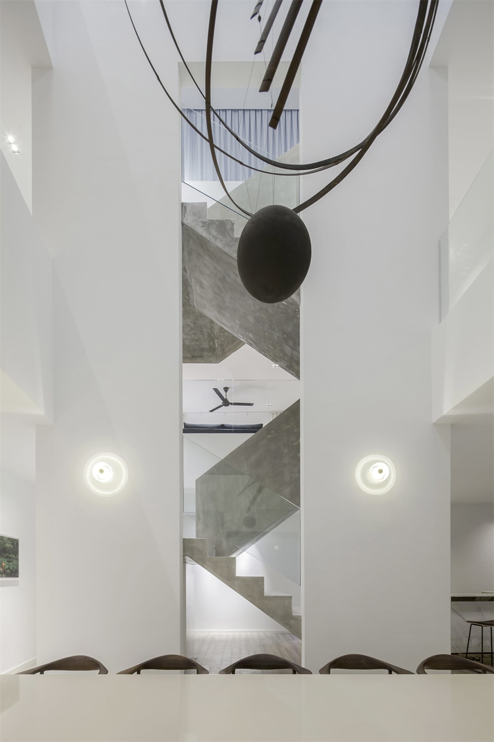 Modern interior design featuring a concrete staircase with a large spherical sculpture hanging above it, set against a minima
