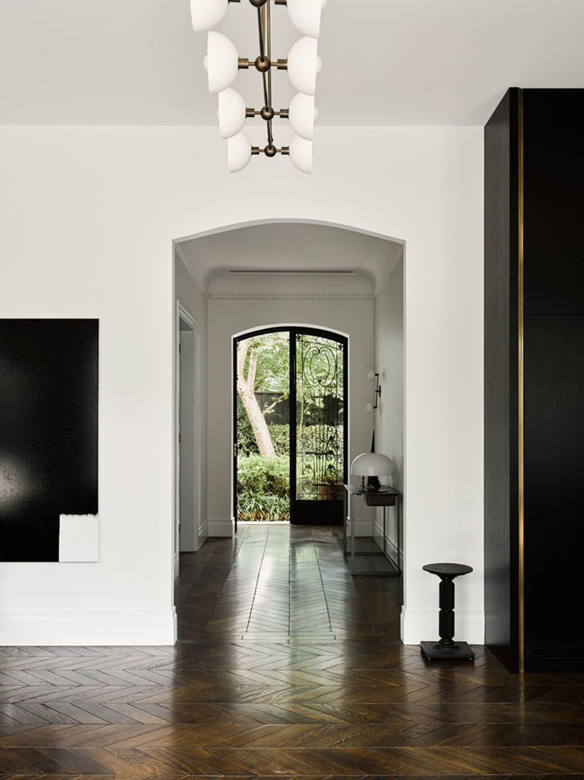 Modern entrance hallway with wooden chevron-patterned flooring, white walls, and a black and white abstract painting.