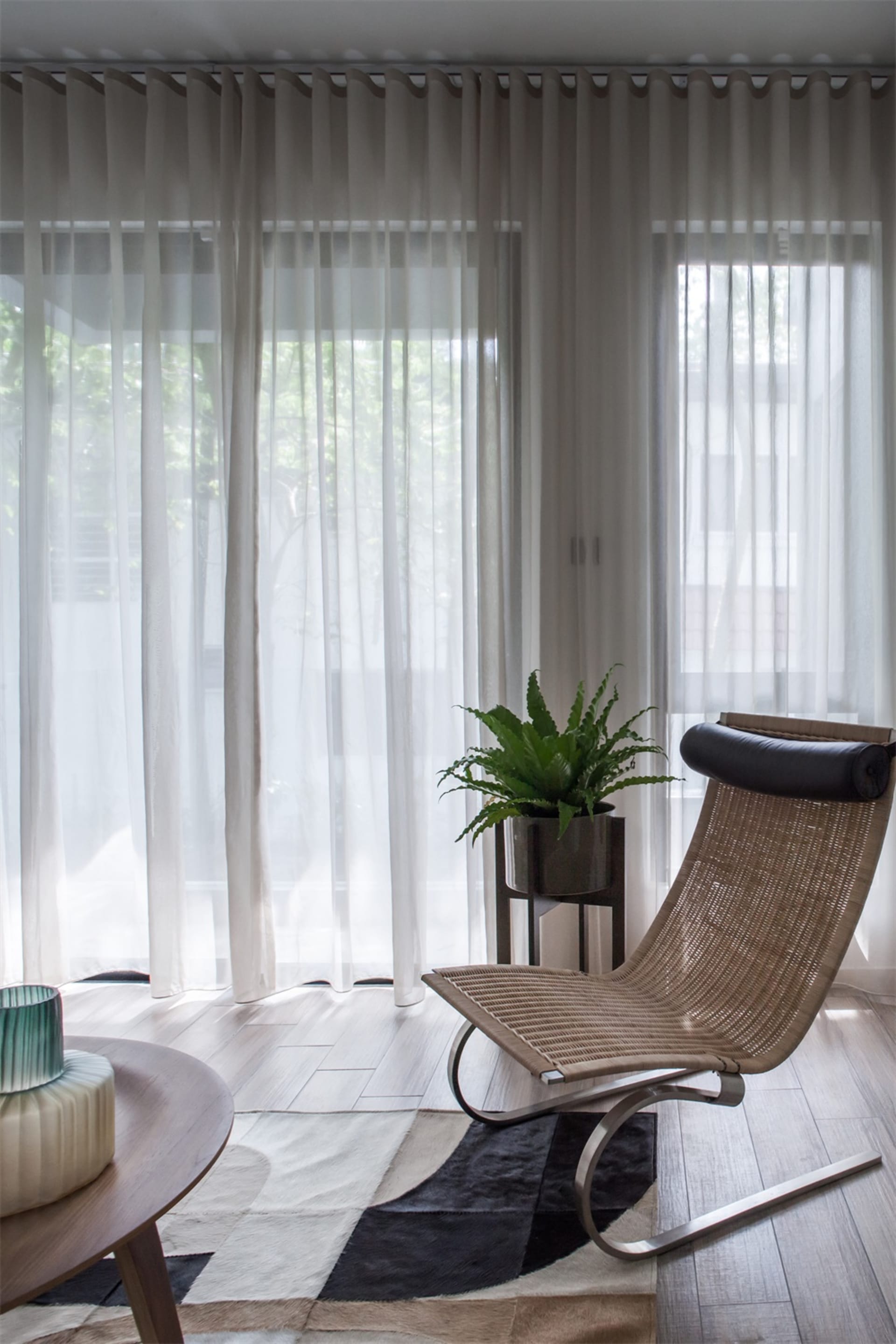 A modern living room with wooden furniture, white curtains, and a plant.