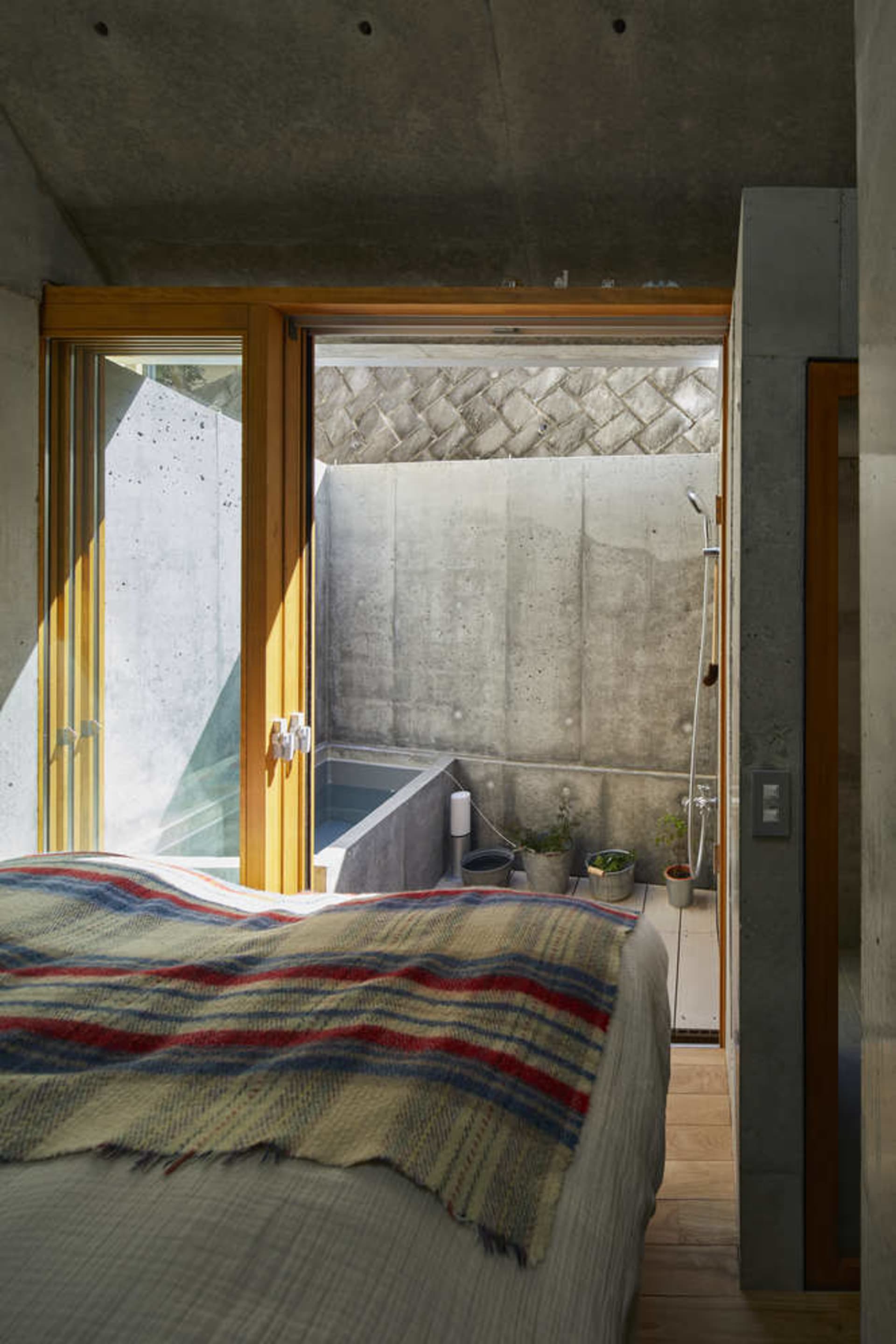 A minimalist bedroom with a concrete wall and wooden floor, featuring a bed with a striped blanket.