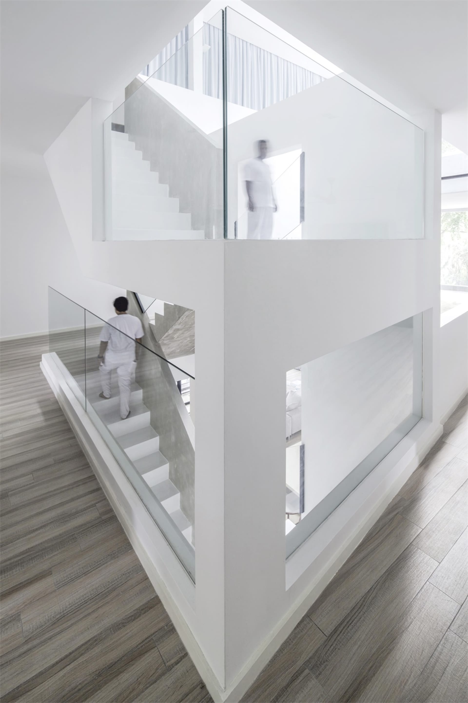 Minimalist, glass staircase interior with white walls and wooden flooring.