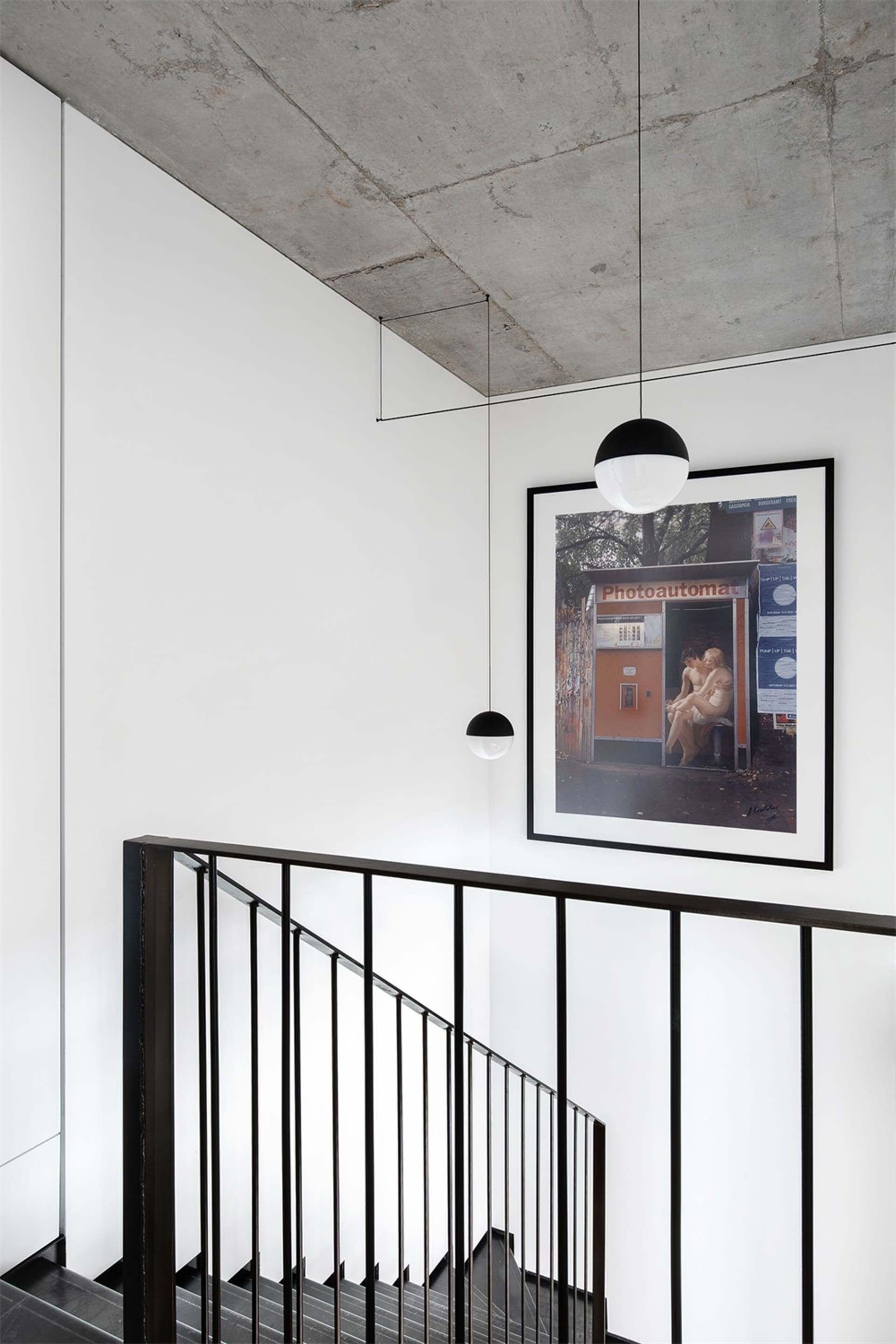 A minimalist industrial staircase with concrete walls and black metal railings, featuring a framed photograph of people in a