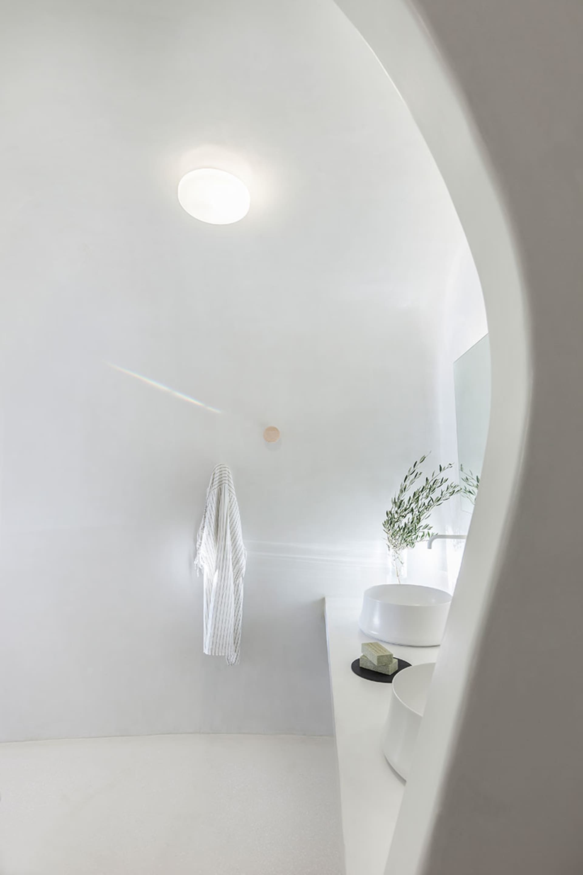 A minimalist bathroom with textured concrete walls and floor, a simple white sink, and a hanging robe.