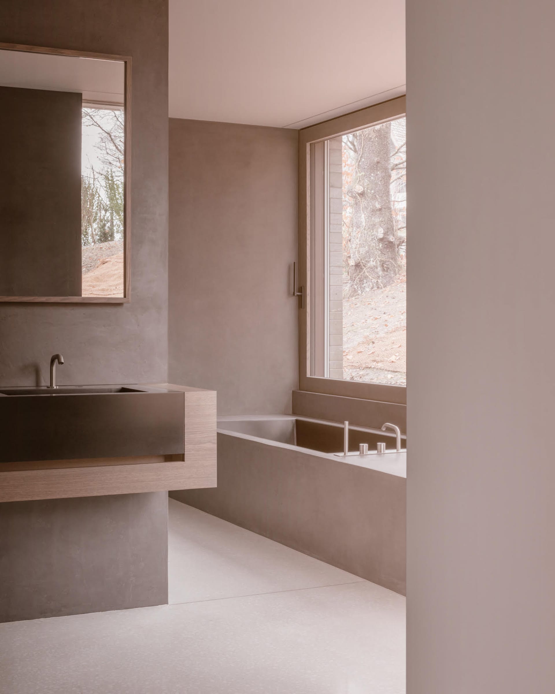 Modern minimalist bathroom featuring concrete walls, wooden vanity, and a large window with a view of the surrounding landsca