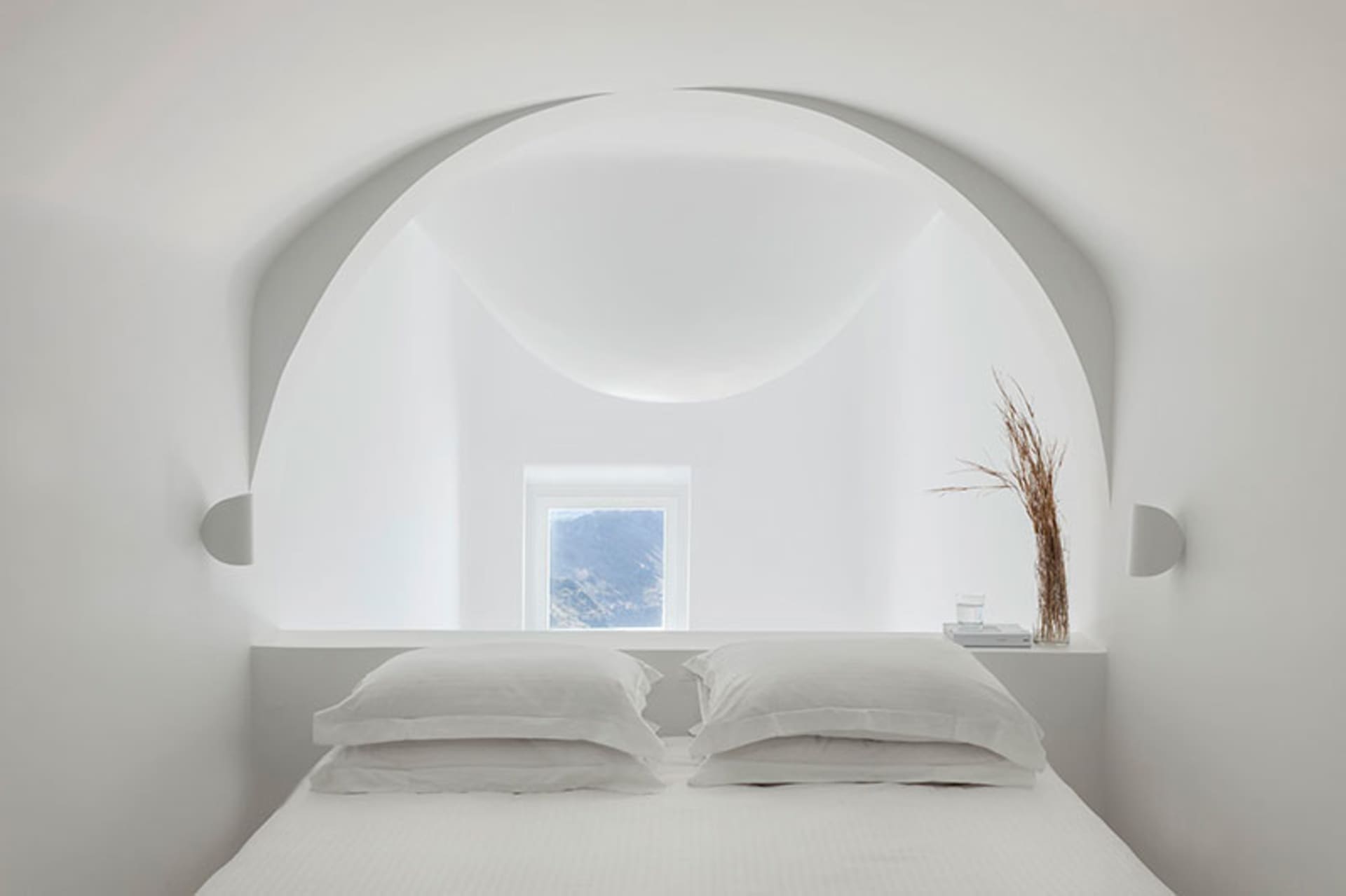 A minimalist bedroom with a white bed, minimalistic decor, and a view through an arched window