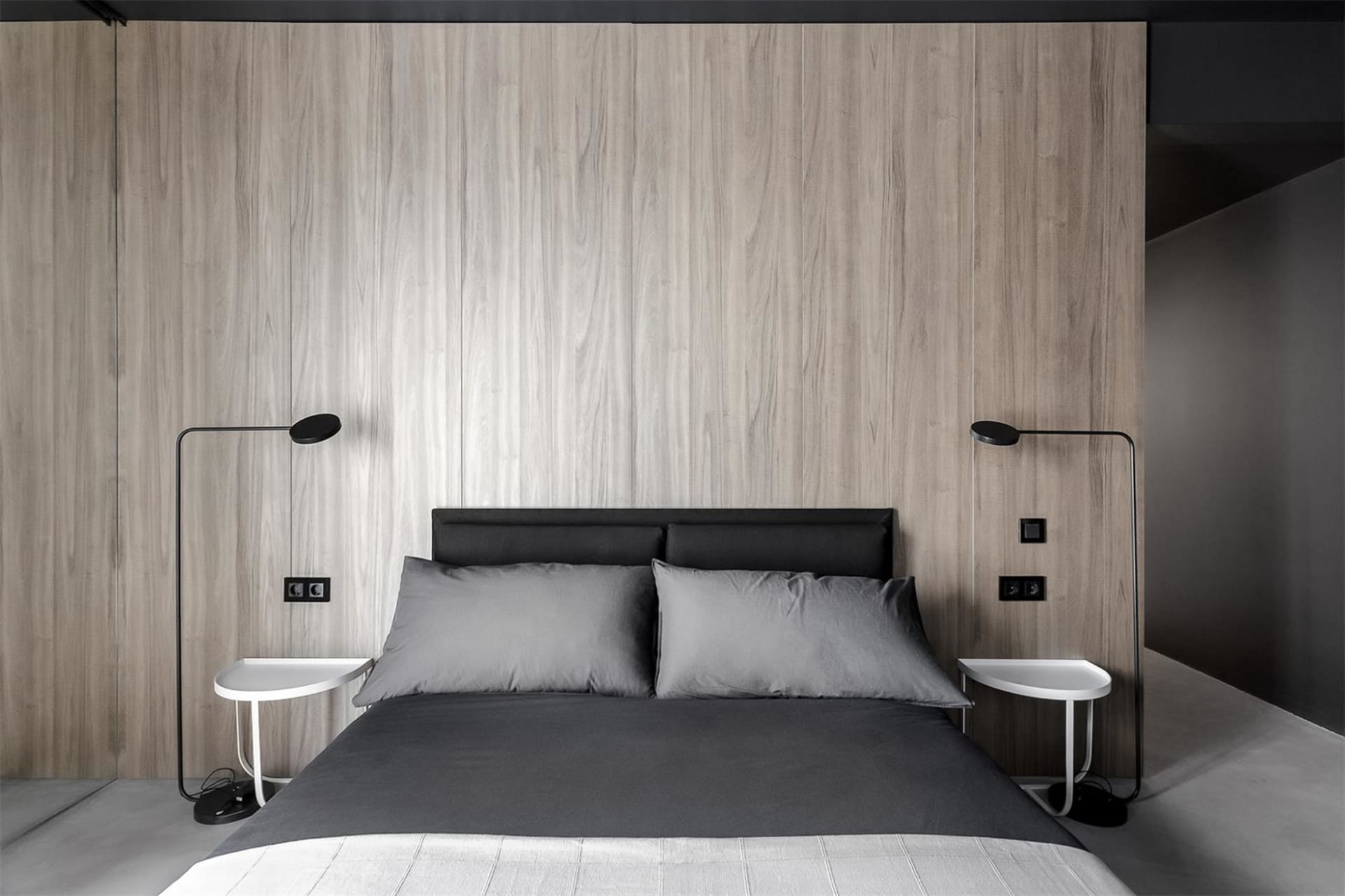Modern bedroom featuring a wood-paneled wall, black bed frame, and gray duvet and pillows.