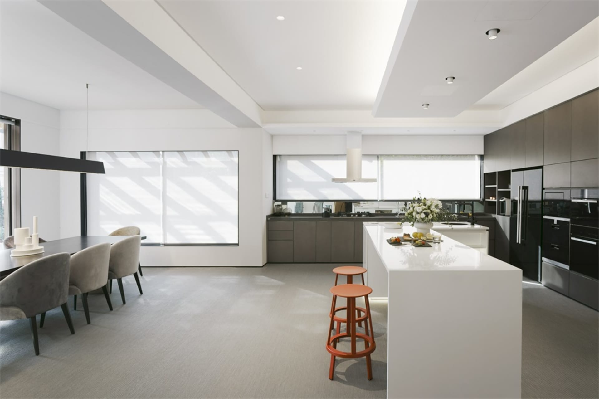A modern residential kitchen with grey and black cabinets, an island with stools, and a dining area with grey chairs.