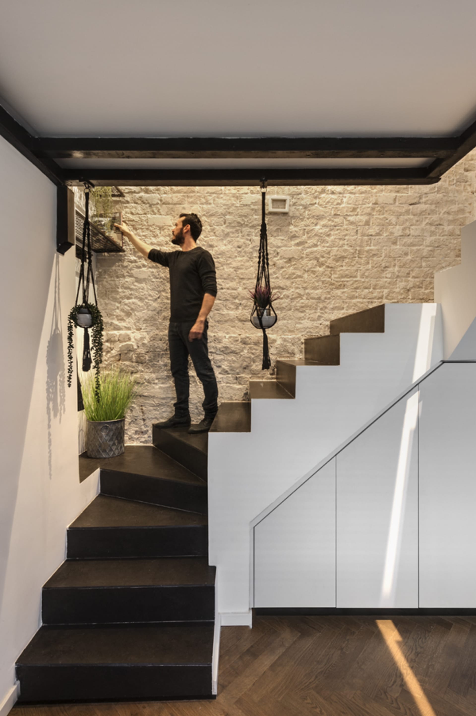 A man standing on a modern staircase made of concrete, with hanging plants.