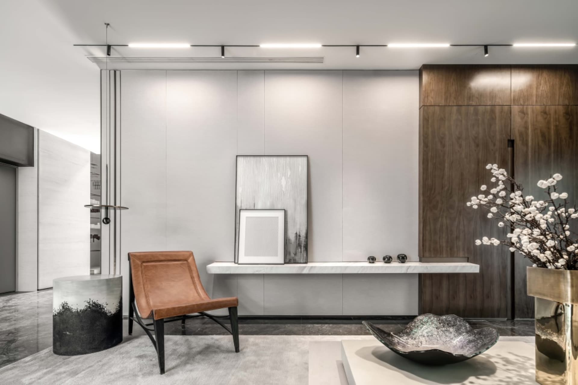 A modern living room with marble finishes, leather accent chair, and wooden cabinets.