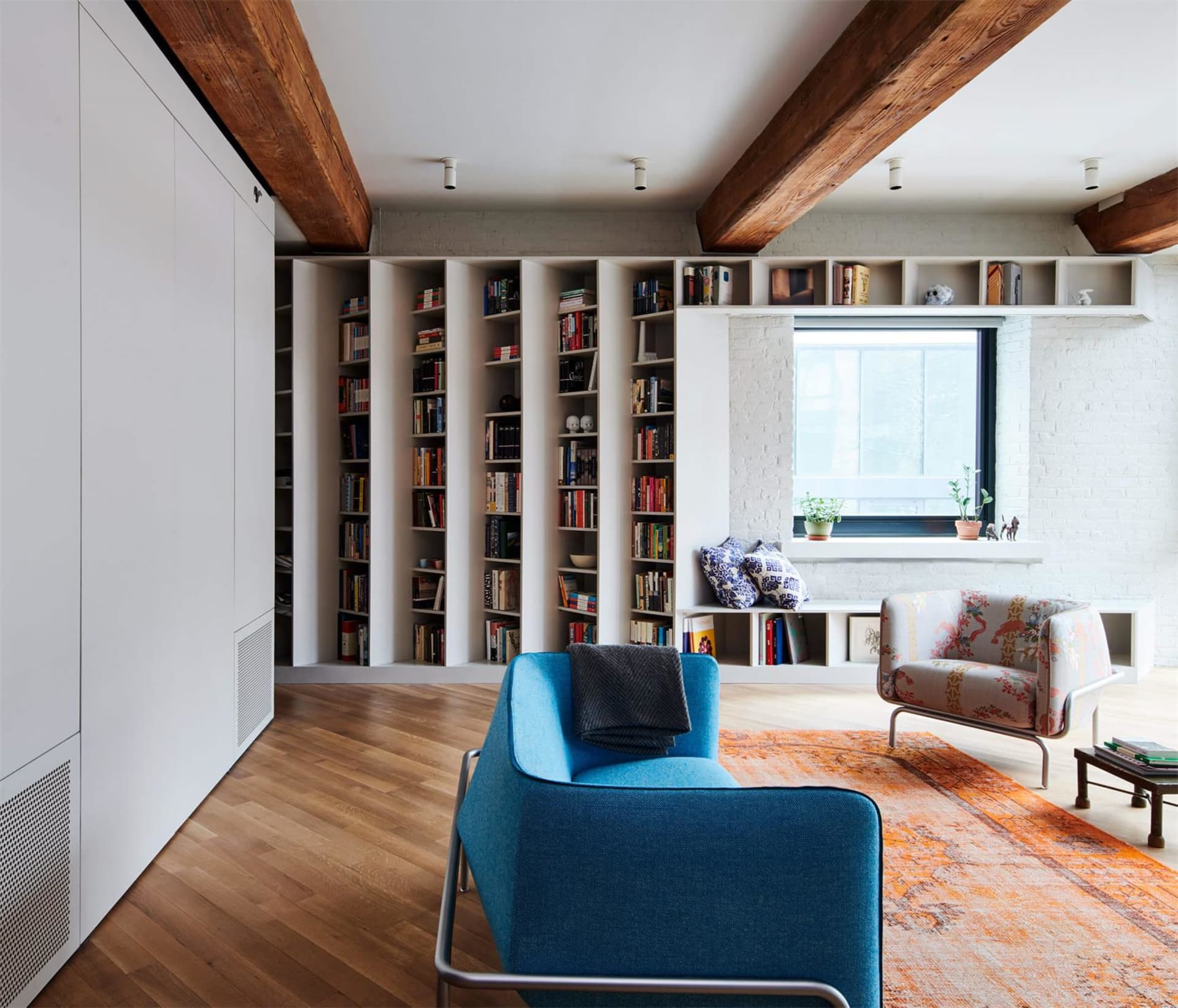 A modern living room featuring wood flooring, concrete walls, glass shelves, and fabric furniture.