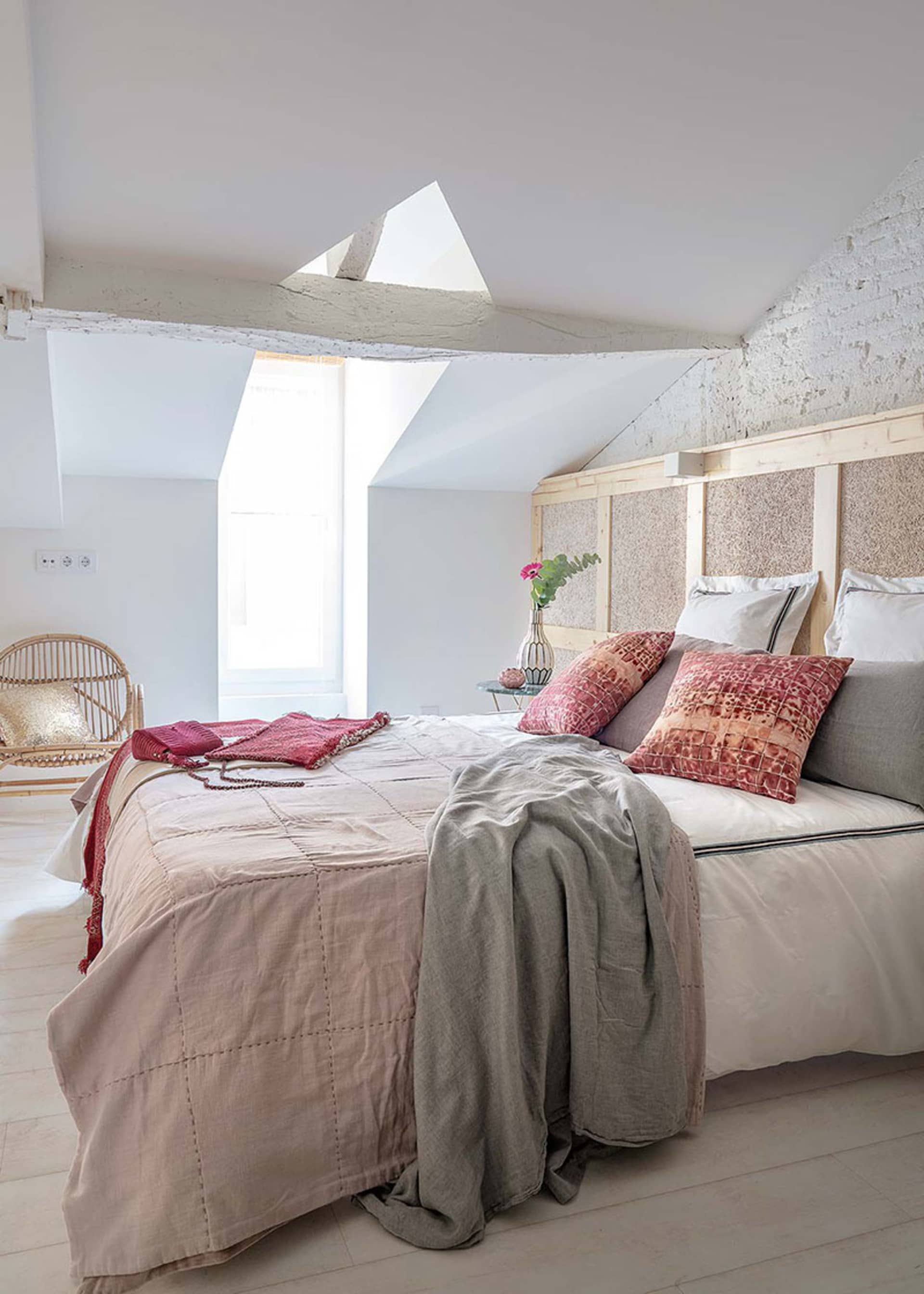 A minimalist bedroom with a textured wood headboard, pink and beige bedding, and a skylight window.