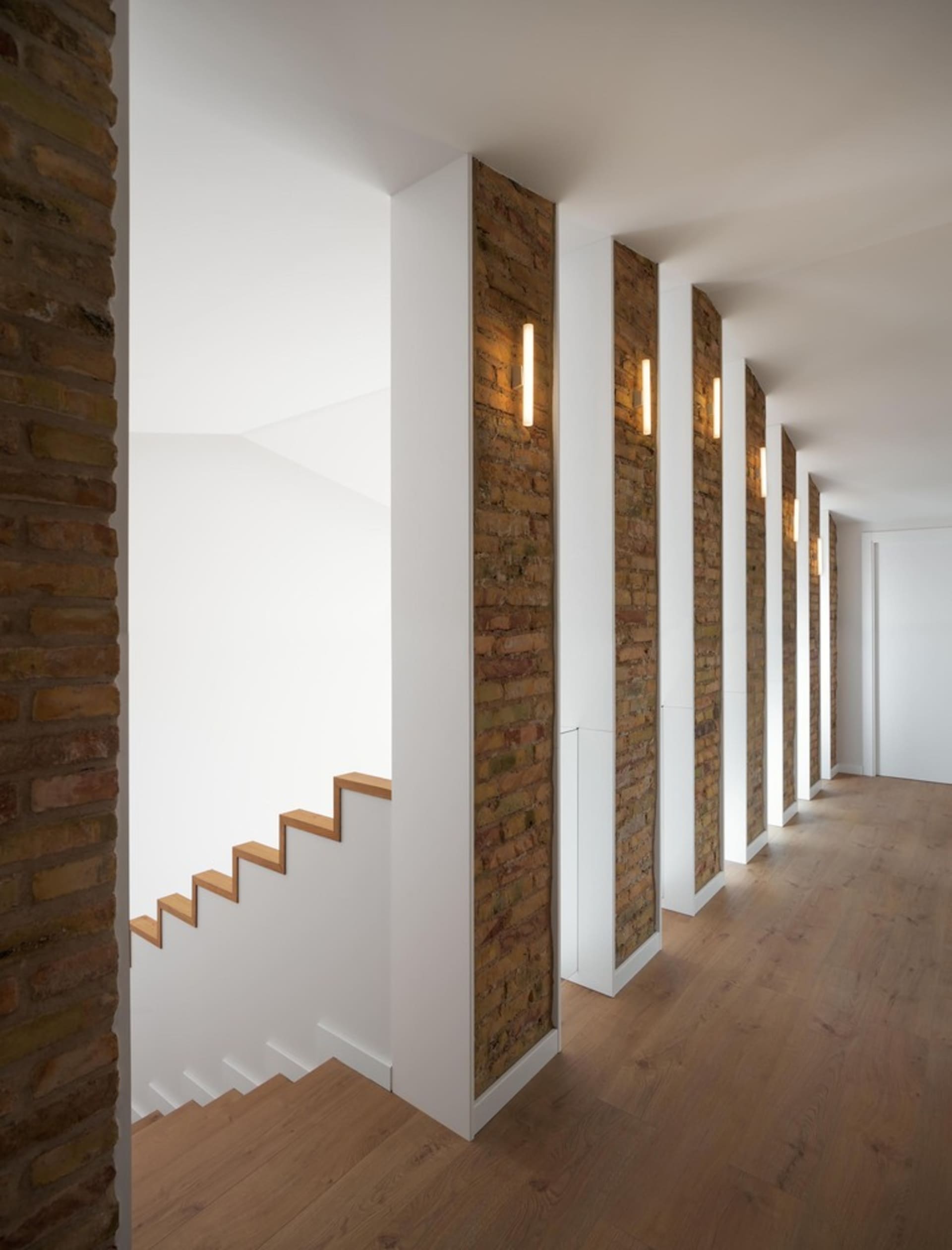 Modern interior design featuring wooden stairs, brick columns, and plaster walls.