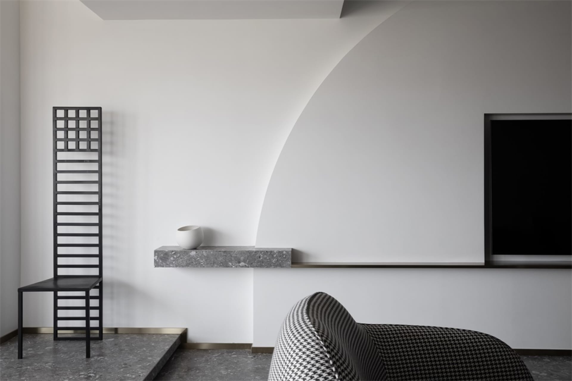 A modern, minimalist living room featuring concrete walls and furnishings, with a black chair, a white bowl, and a black, pat