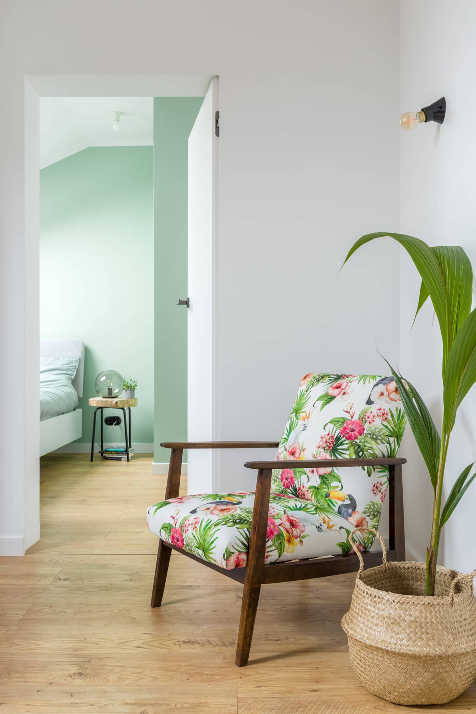 A modern tropical-themed living room featuring a wooden armchair with a floral and bird print cushion, a woven basket with a