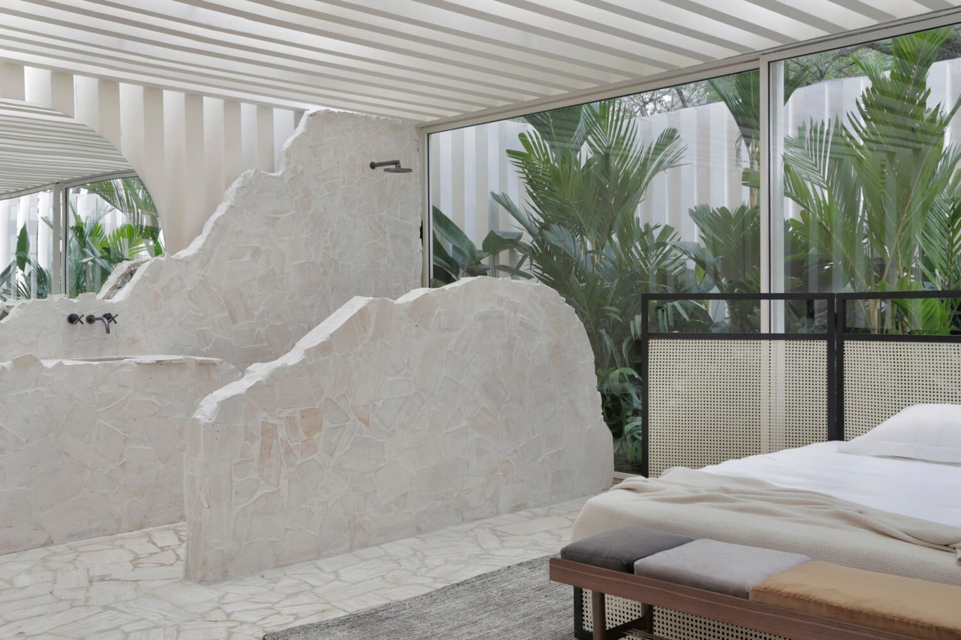 A minimalist bedroom featuring a stone tub and greenery outside.