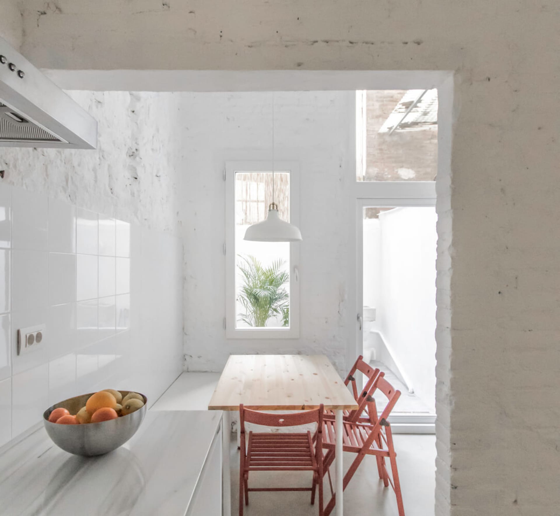 Modern minimalist kitchen with marble countertops and wooden dining table and chairs.