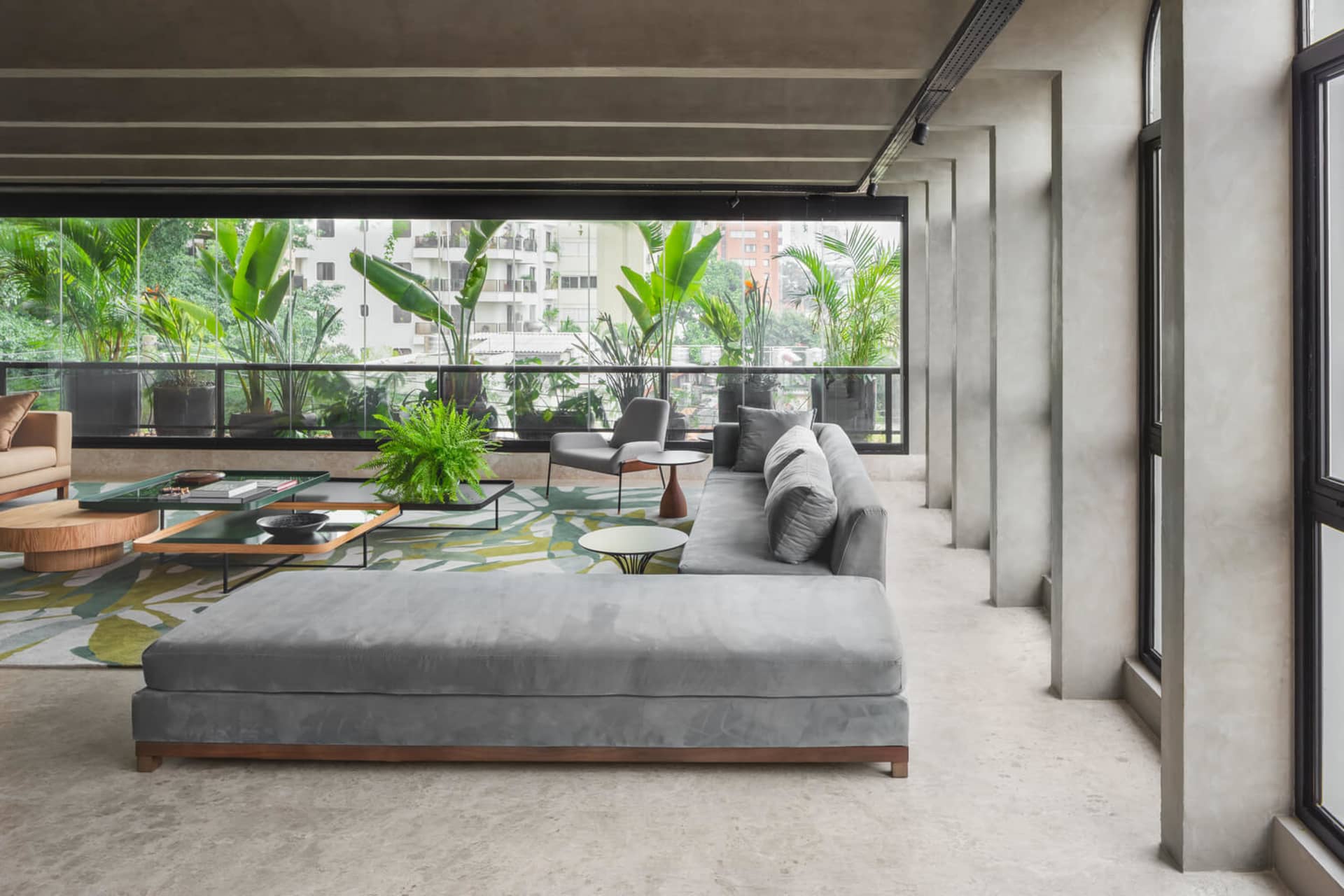 Modern living room with concrete furniture, large windows, and green plants.