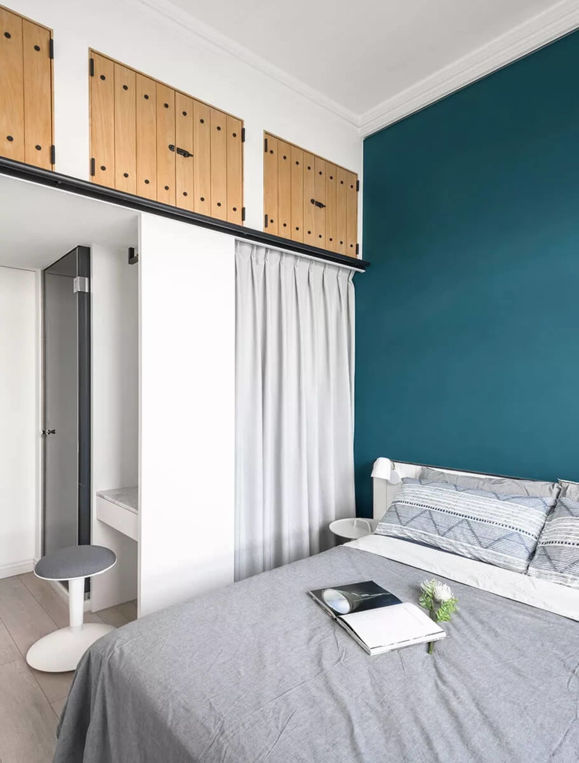 A minimalist bedroom featuring a grey bed with white fabric bedding and wooden accents.