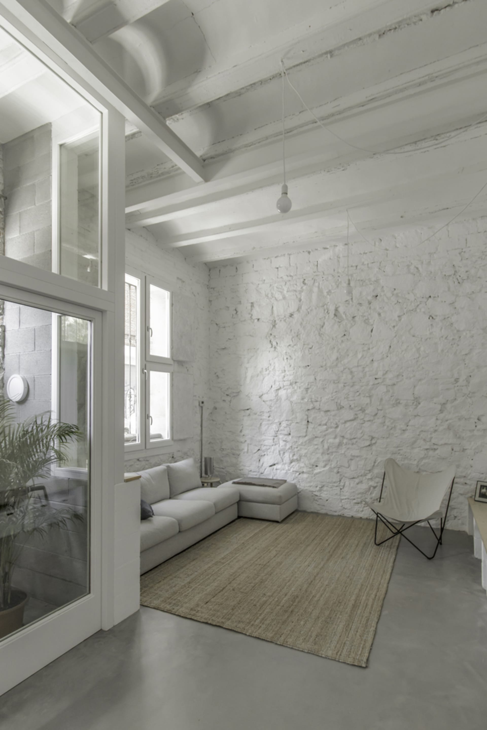 Minimalist living room with concrete walls and floor, featuring a white couch and a woven rug.