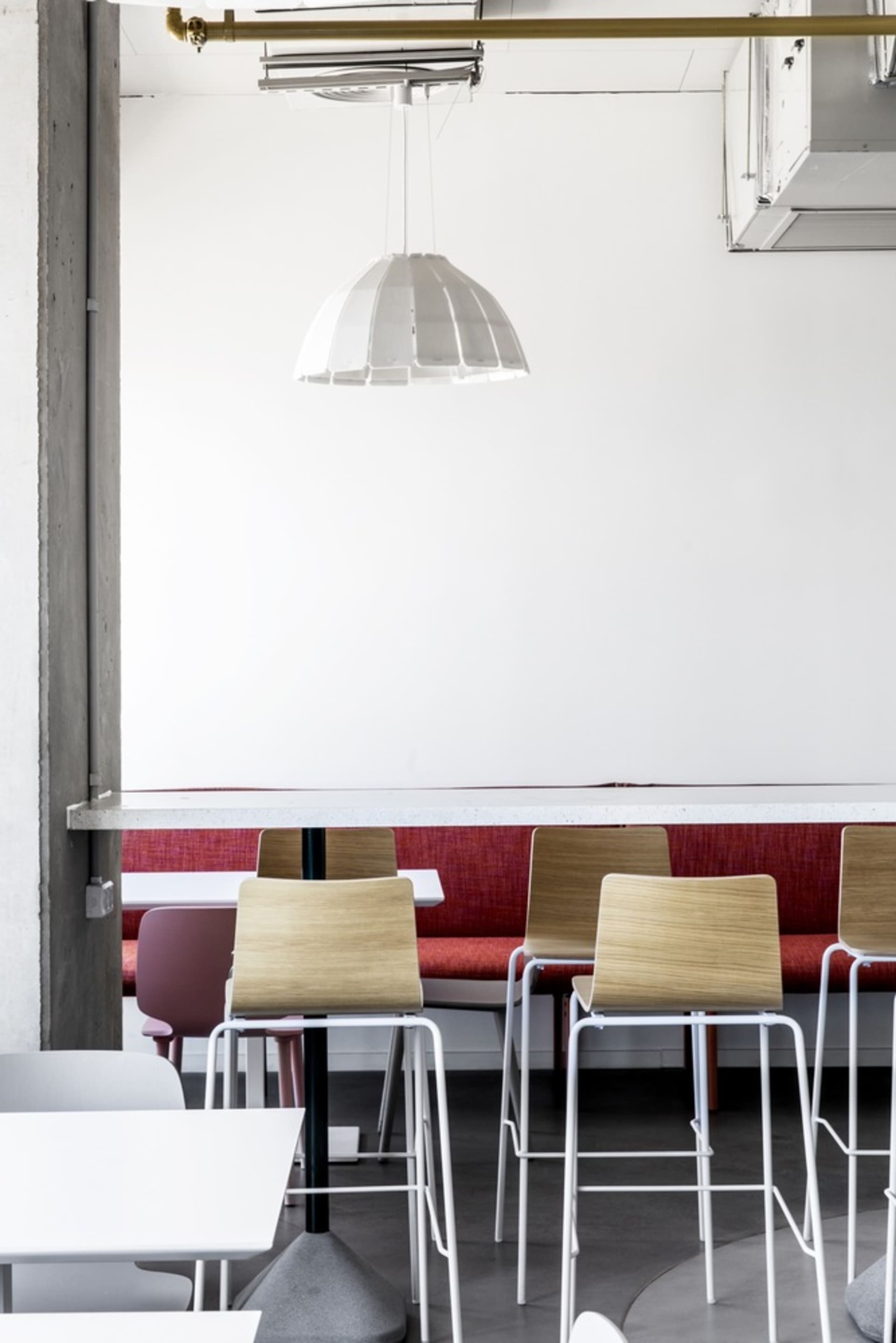 White pendant light above a long red bench seat in a modern cafe interior design.