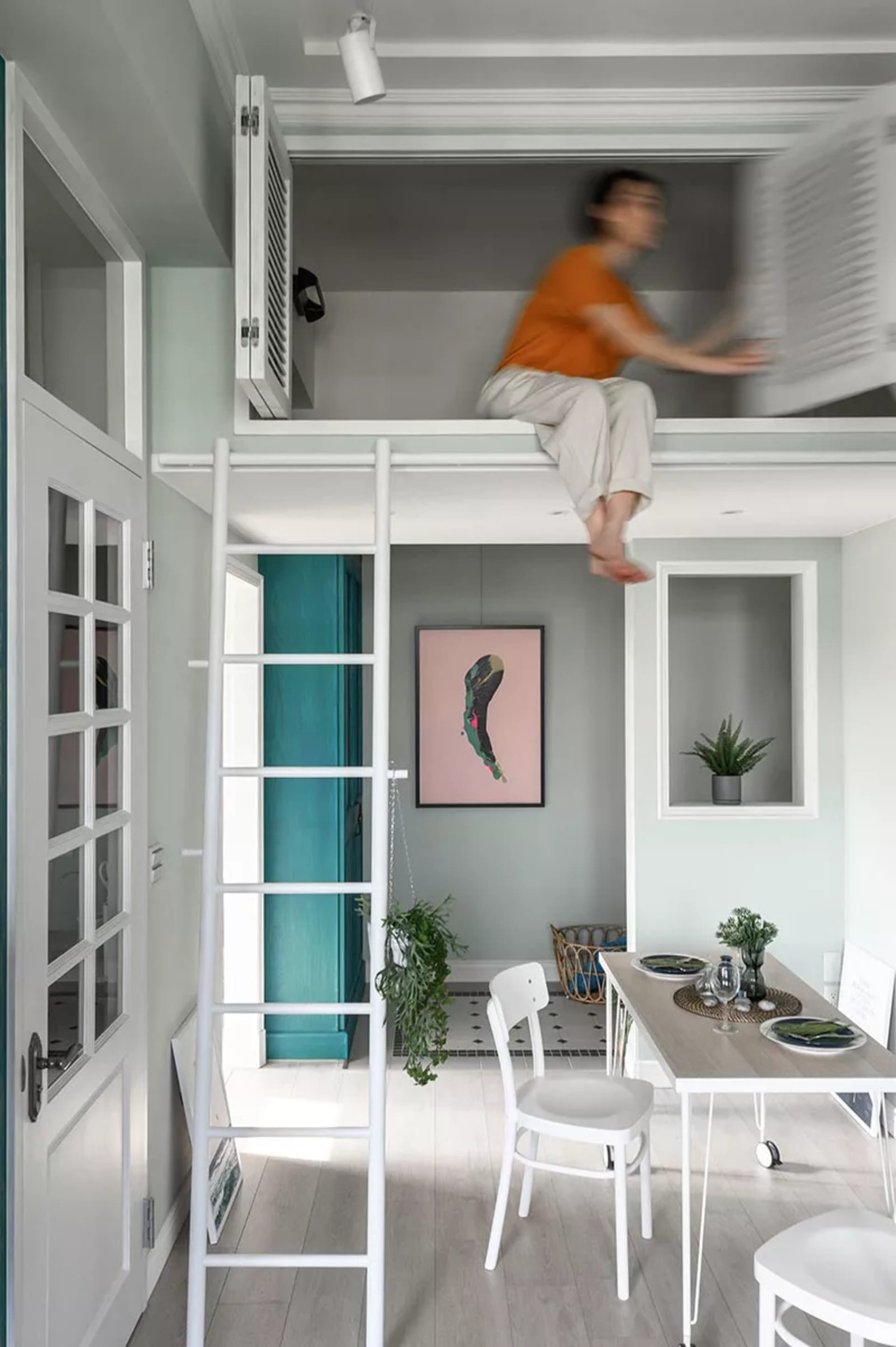 Minimalist design featuring a concrete loft with a white ladder, a dining table, and a person sitting on the loft.