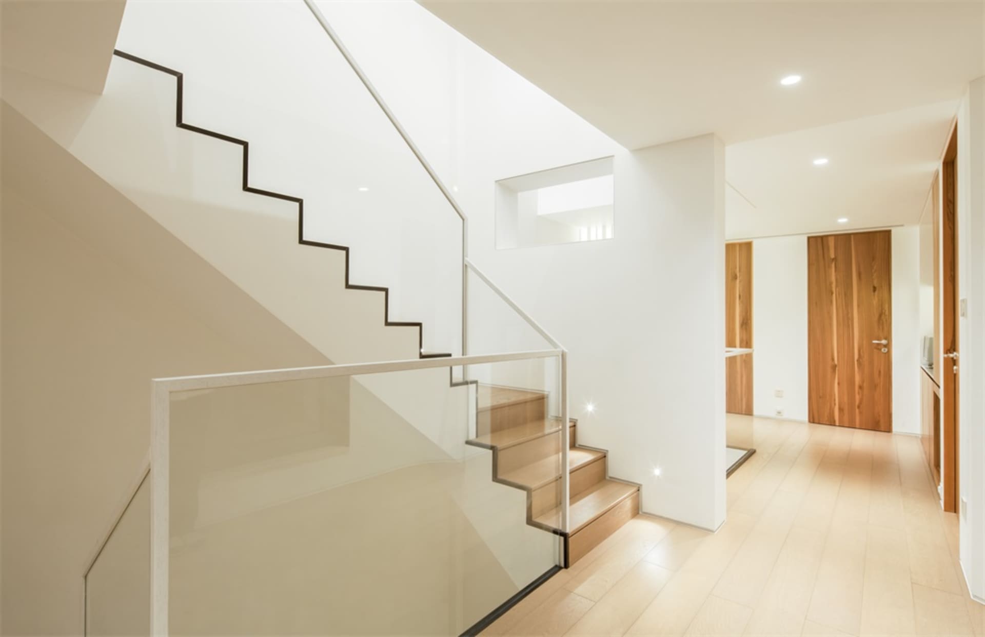 Modern interior featuring a glass staircase with white walls and wooden flooring.