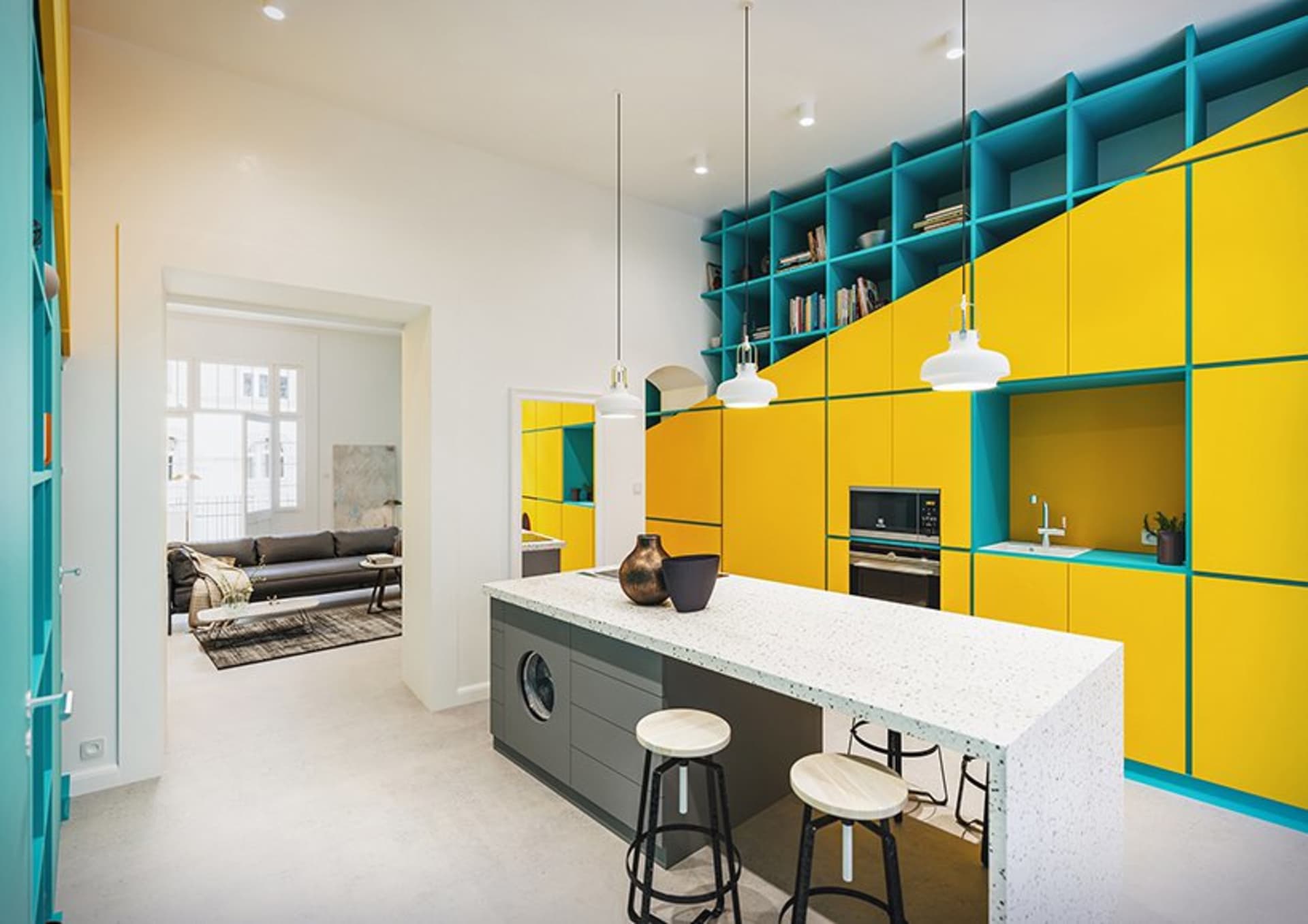 Modern kitchen with yellow and teal cabinets, white countertops, and pendant lights.