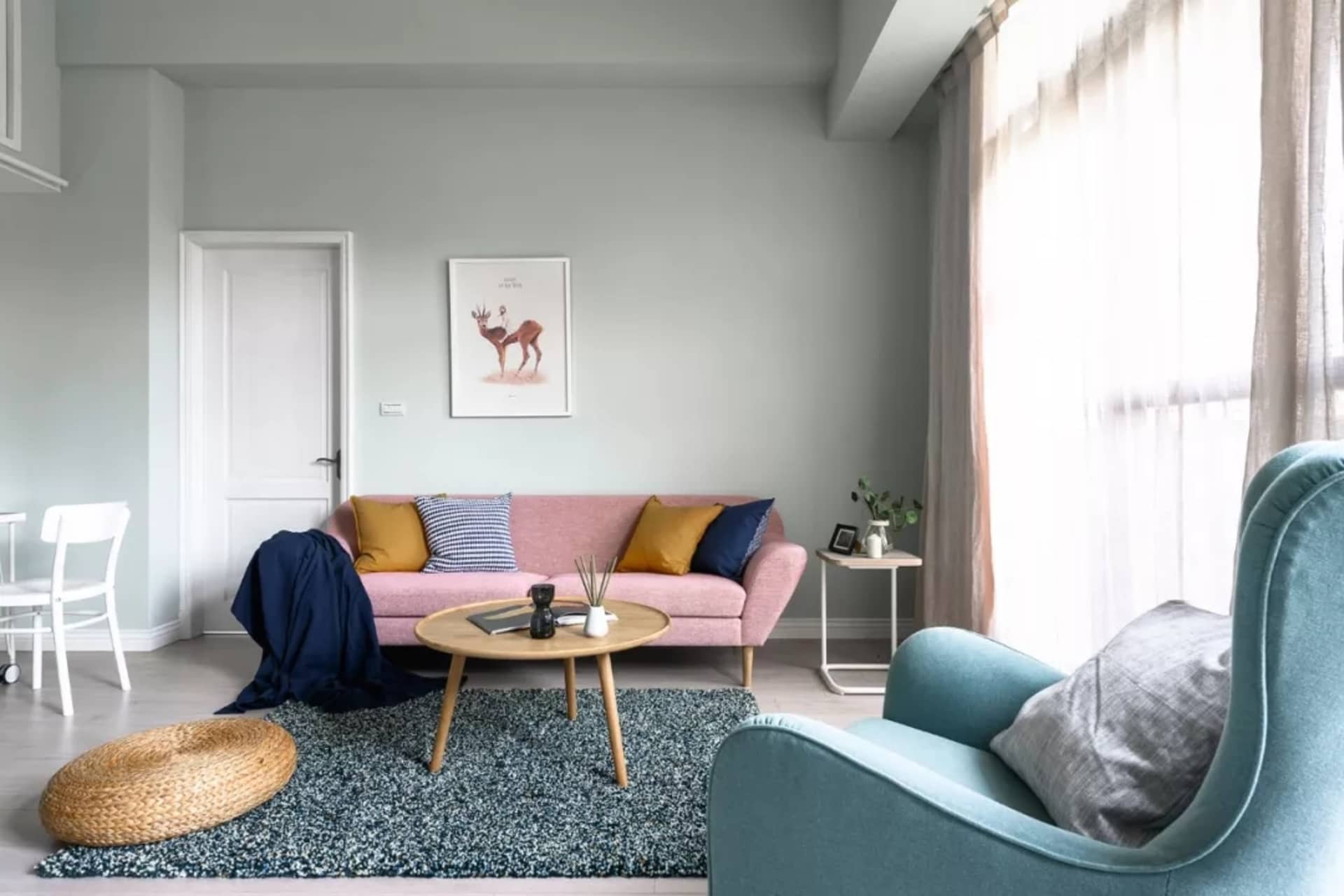 Scandinavian living room featuring a blue and pink couch with cushions, a wooden coffee table, a round stool, framed deer art