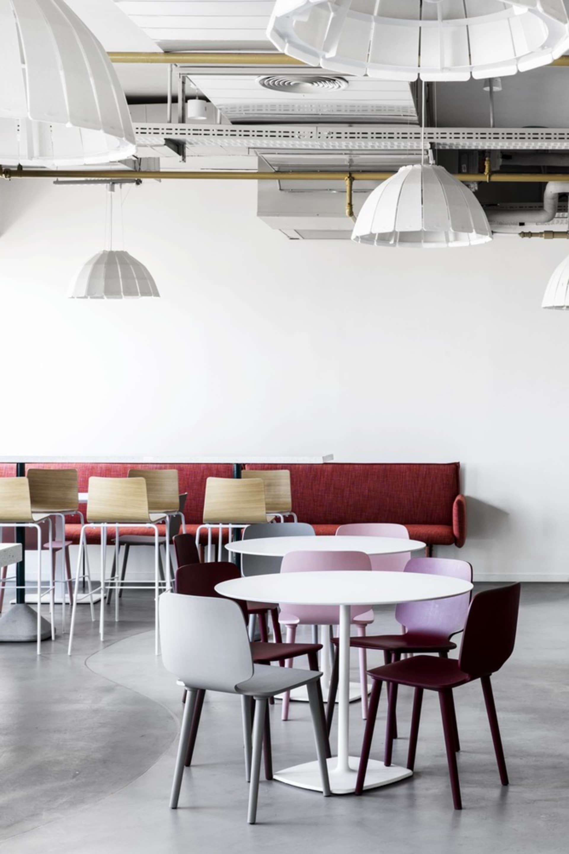 A modern restaurant interior with white tables, colorful chairs, and a red bench seating area.