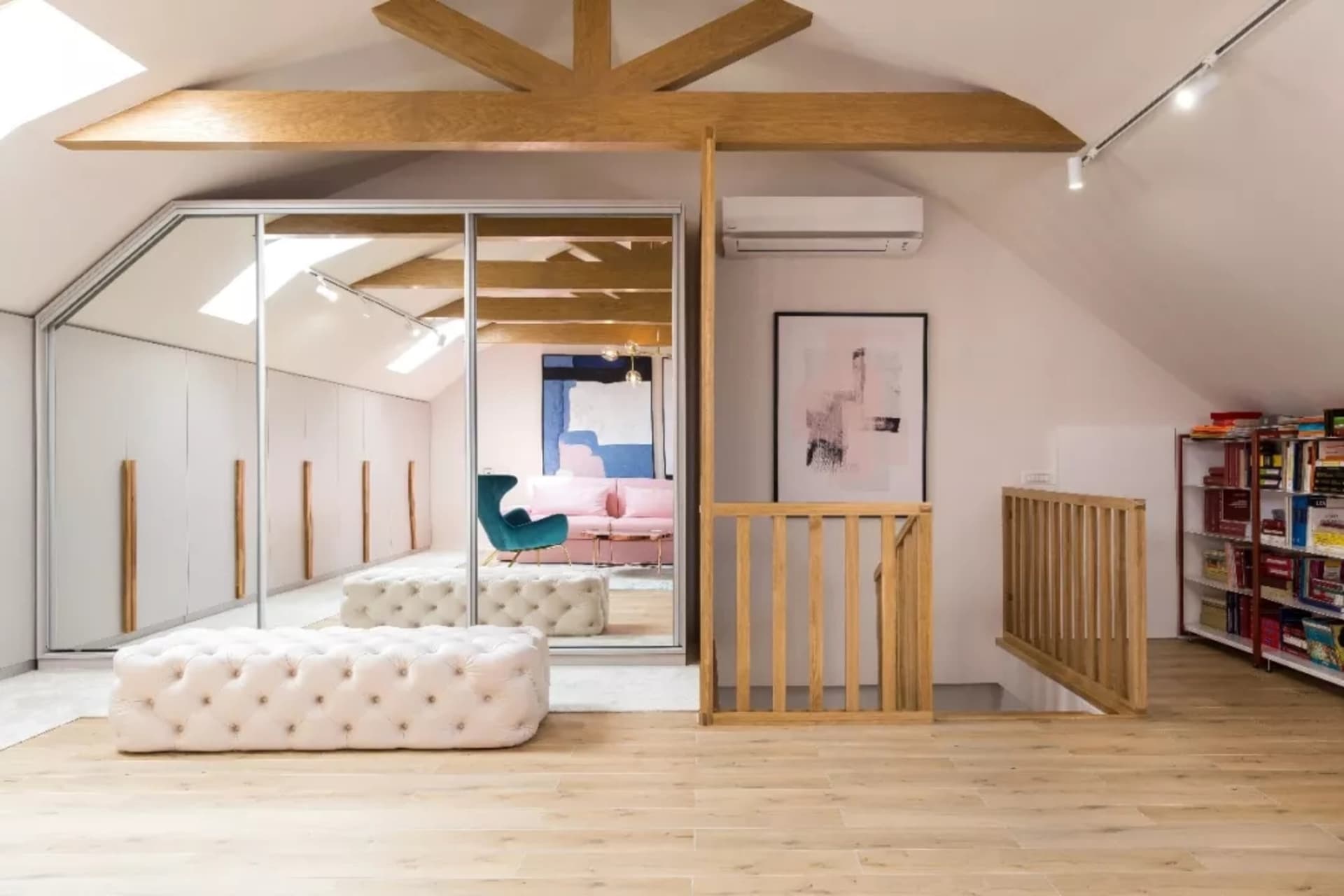 A modern interior design featuring wood flooring, a white tufted ottoman, a teal armchair, a pink sofa, and a wooden balcony