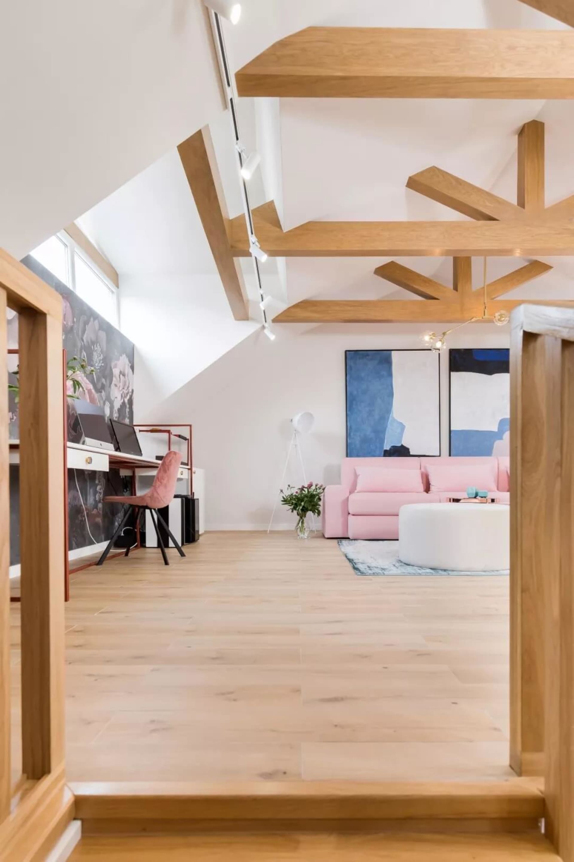 A modern living room featuring a pink couch, white ottoman, and wooden beams on the ceiling.